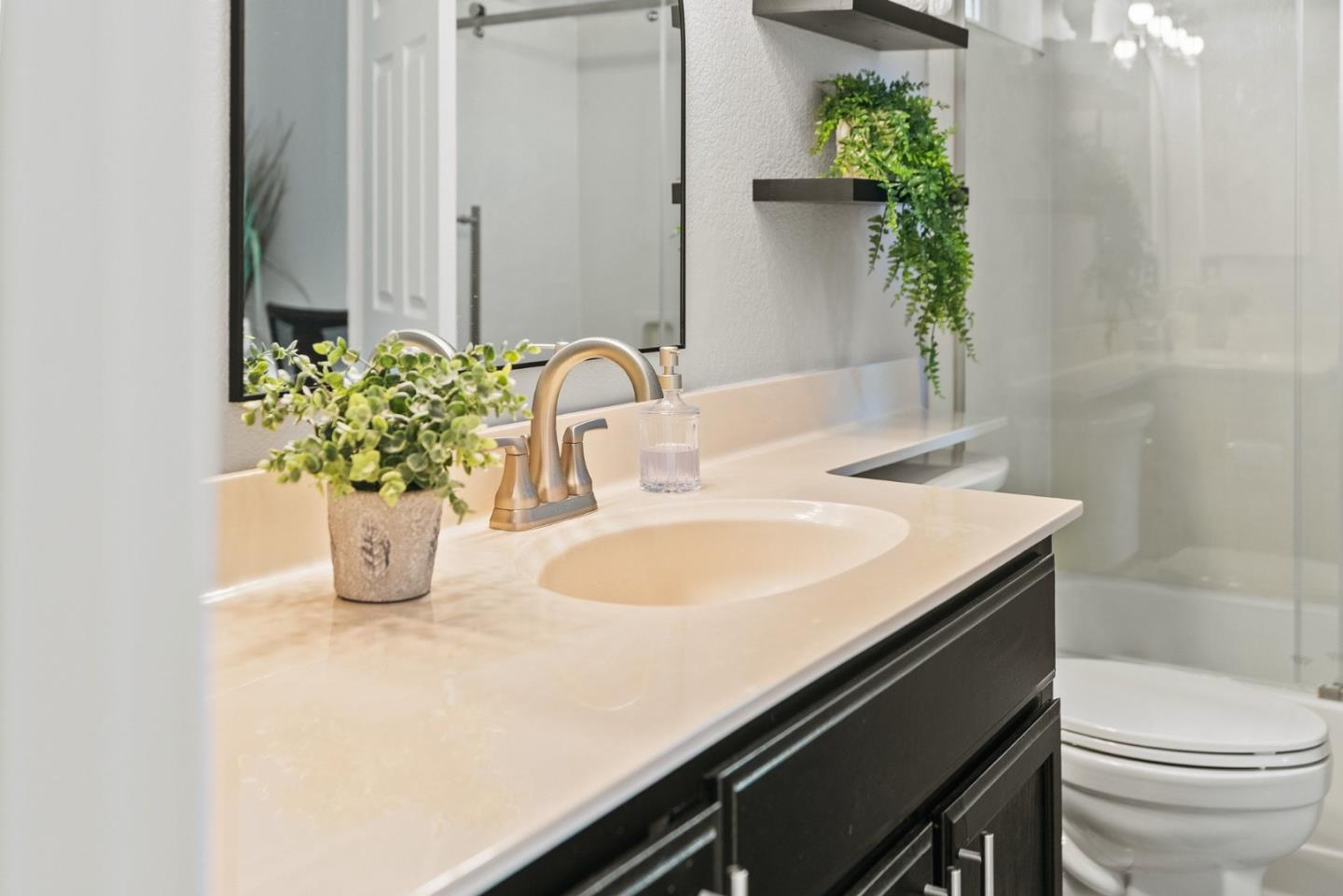 Bathroom vanity with a light stone countertop, inset sink, dark cabinets, and glass-enclosed tub and shower.
