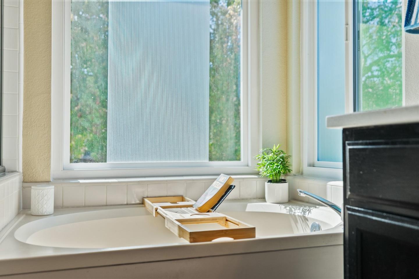 Bathroom soaking tub beneath large windows, with a wooden bath tray and potted plant.