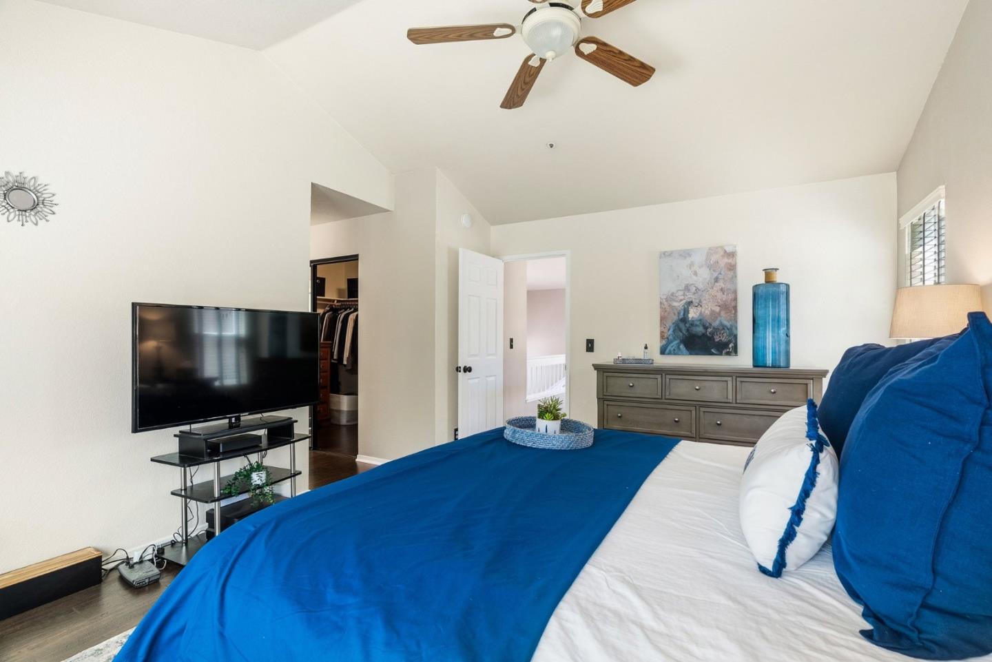 Bedroom with vivid blue bedding, a ceiling fan, television, and gray dresser.