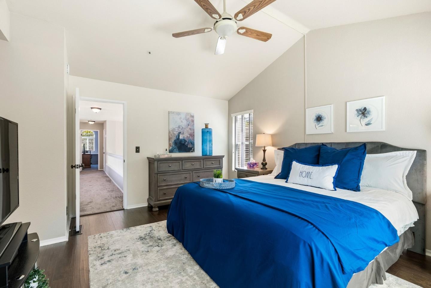 Bedroom with a blue-and-white bed, gray upholstered headboard, and ceiling fan.