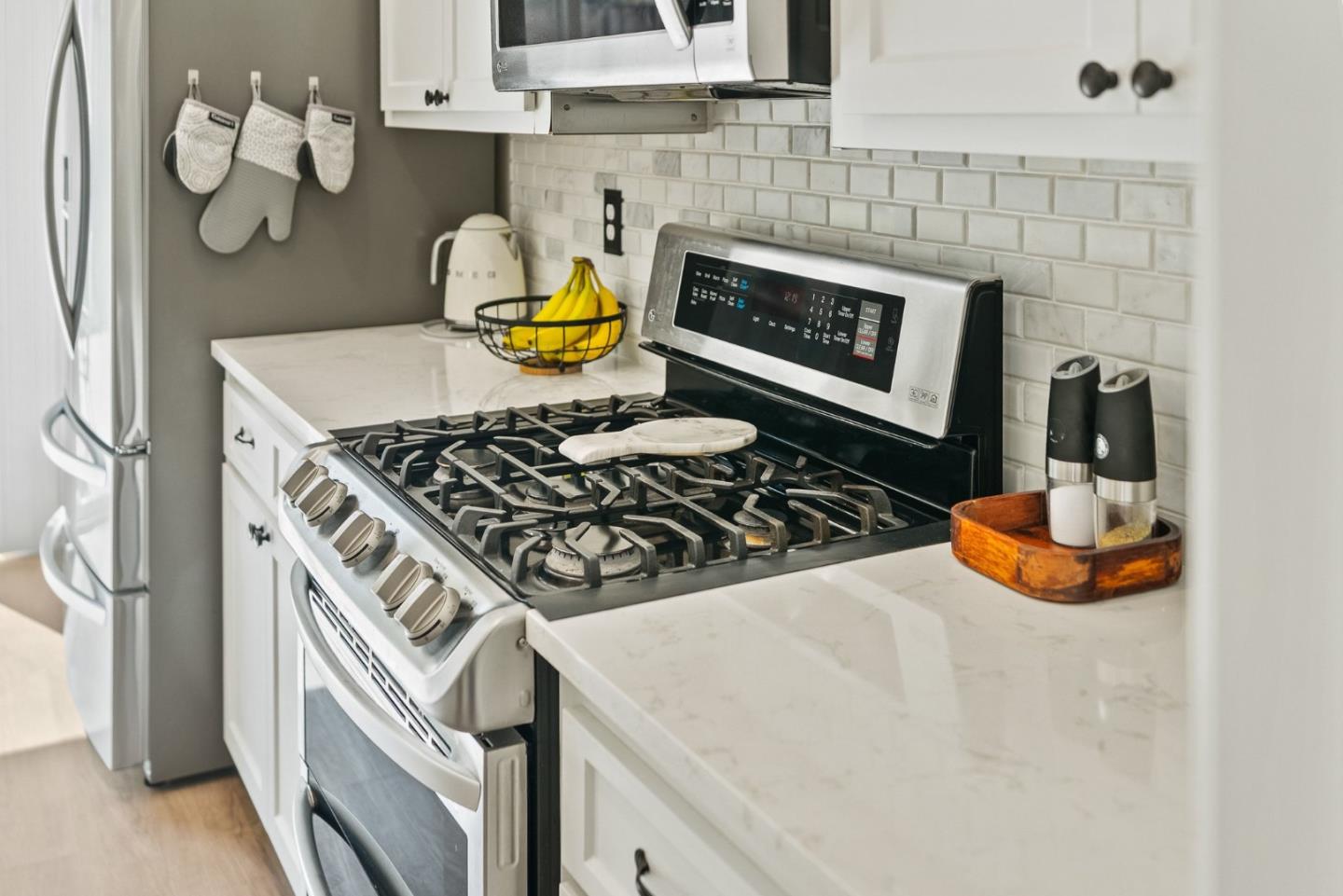 Kitchen with a stainless gas range, white cabinetry, and light stone counters.