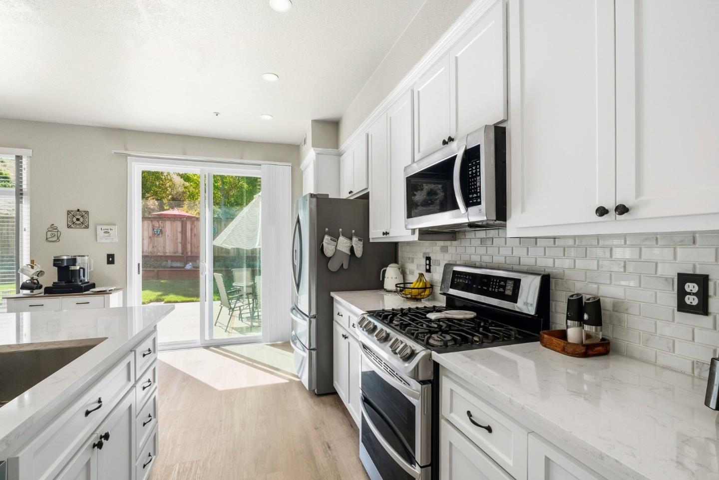Bright kitchen with white cabinetry, stone counters, stainless appliances, and a sliding glass door to the backyard.