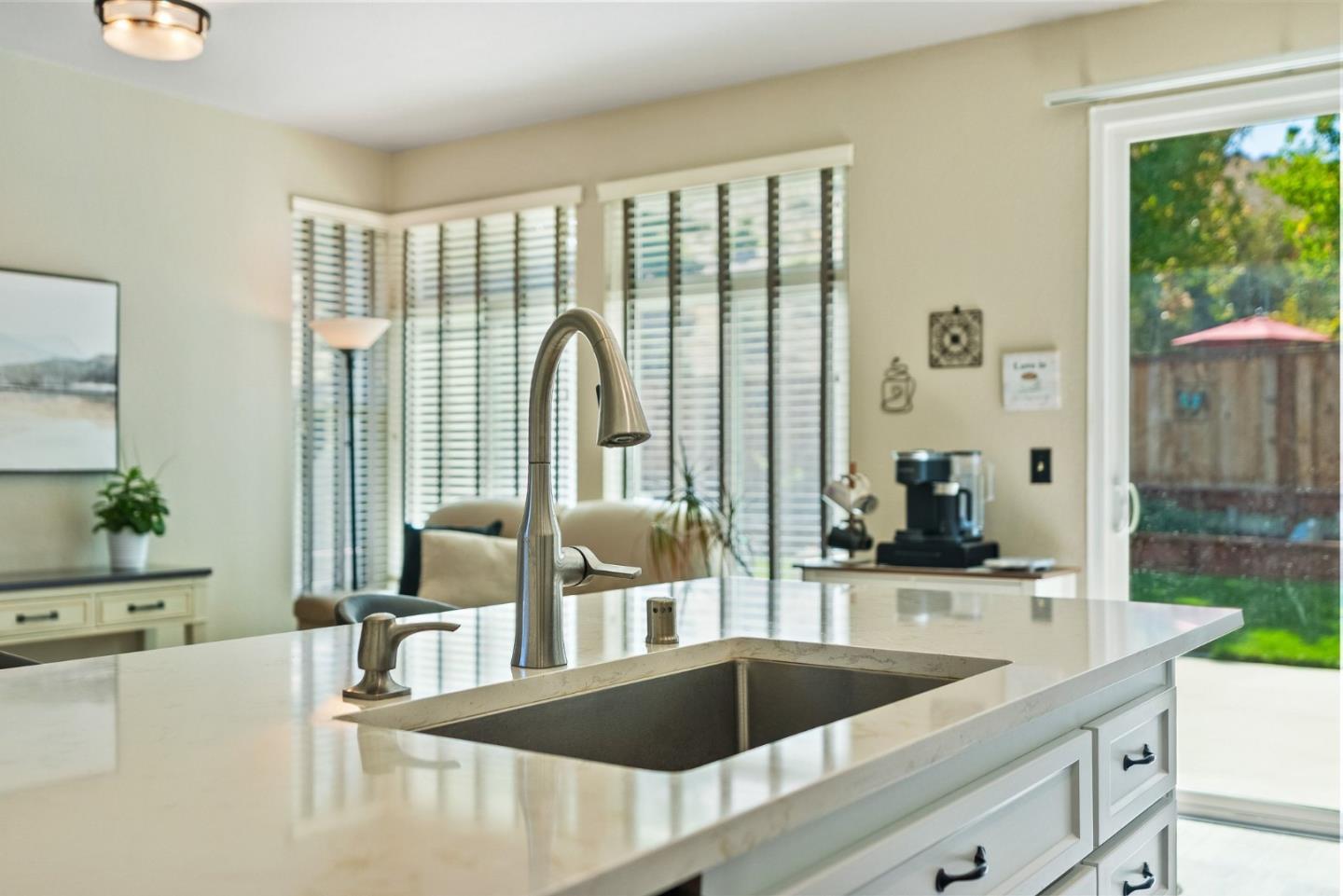 Kitchen island with a white stone countertop, undermount sink, and tall faucet beside a sliding glass door.