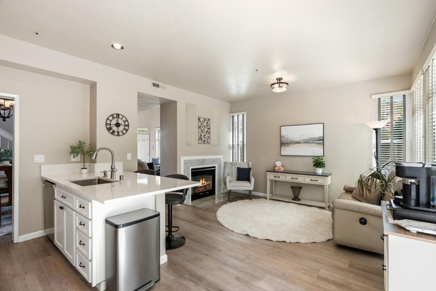 Open-plan kitchen and living room with a white island, fireplace, and large windows.