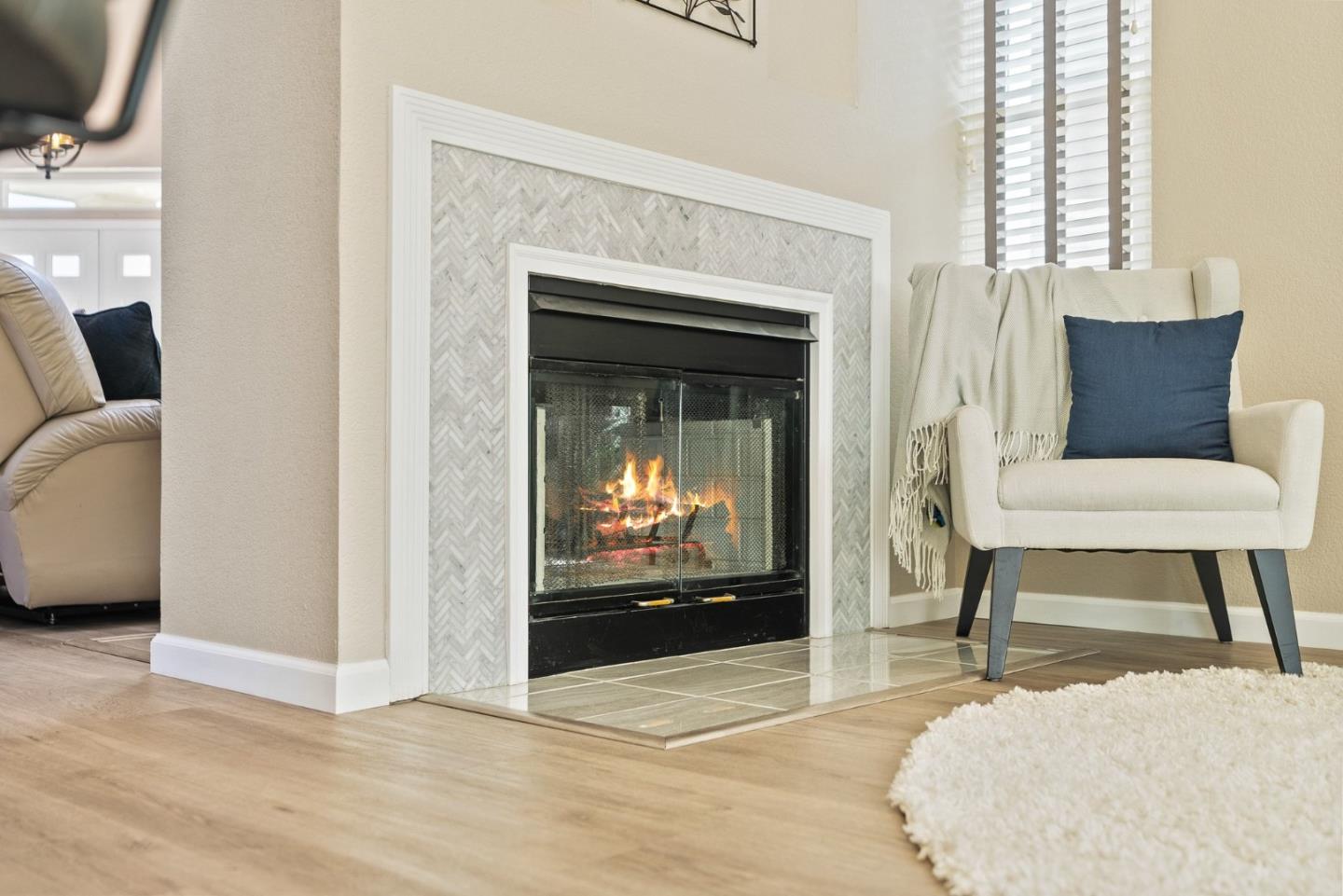 Living room fireplace with a herringbone tile surround, burning fire, and cream armchair.