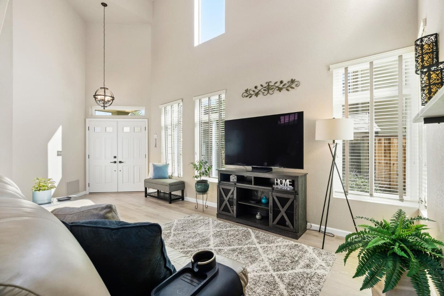 Vaulted living room with white double doors, tall windows, a television, and a light sofa.