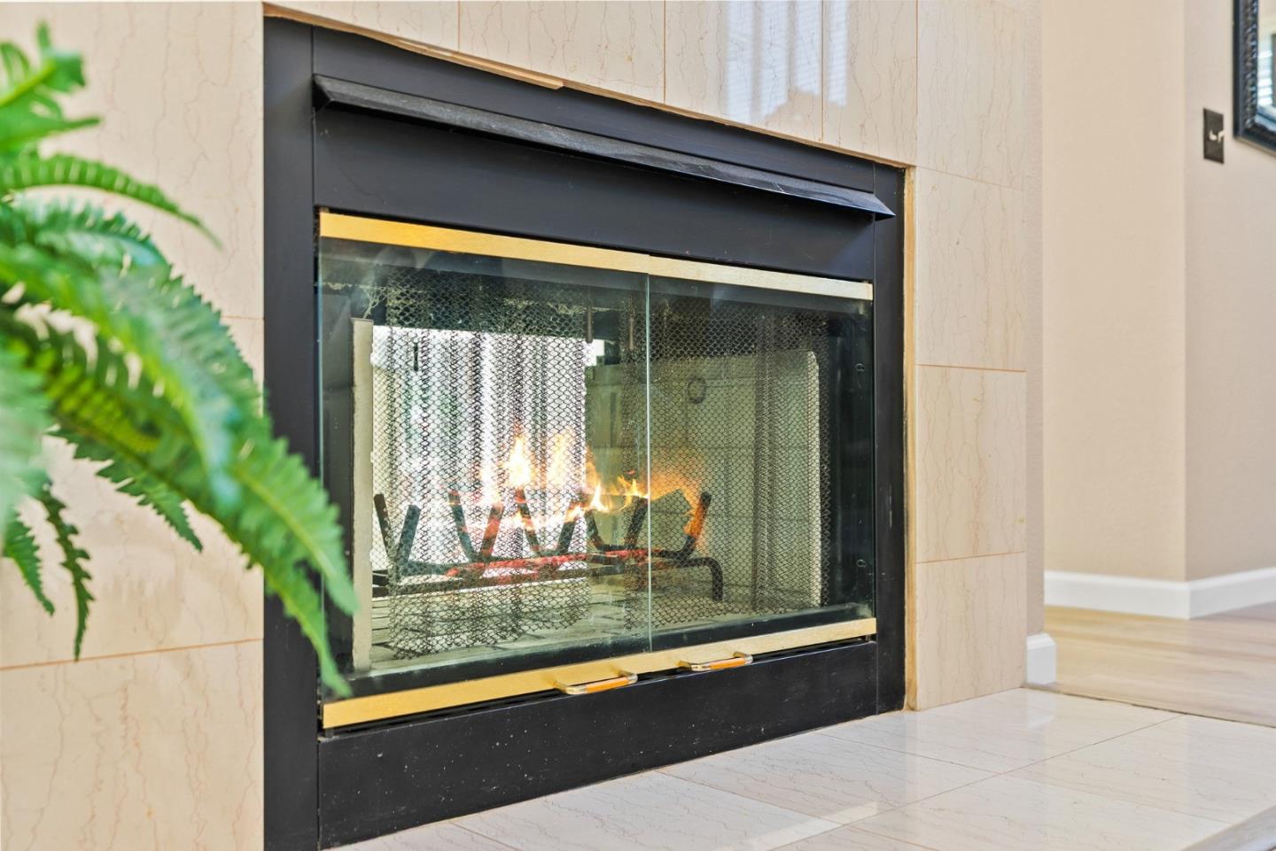 Lit fireplace with black frame and brass trim in a cream marble-tile surround.