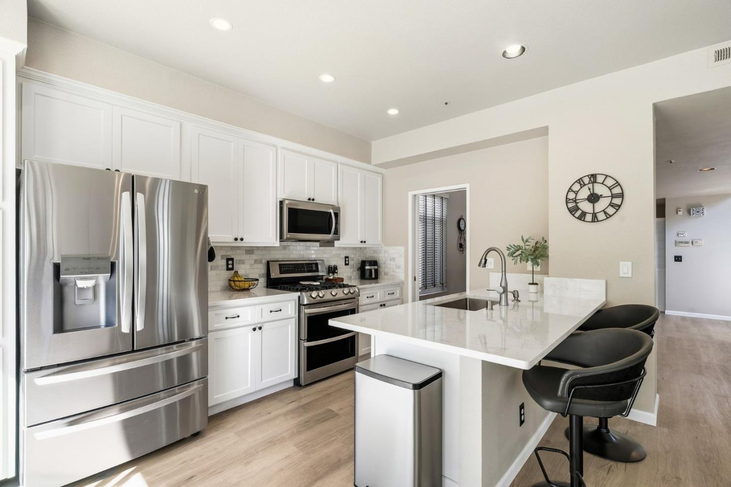 Bright kitchen with white cabinets, stainless steel appliances, and a large island with black bar stools.