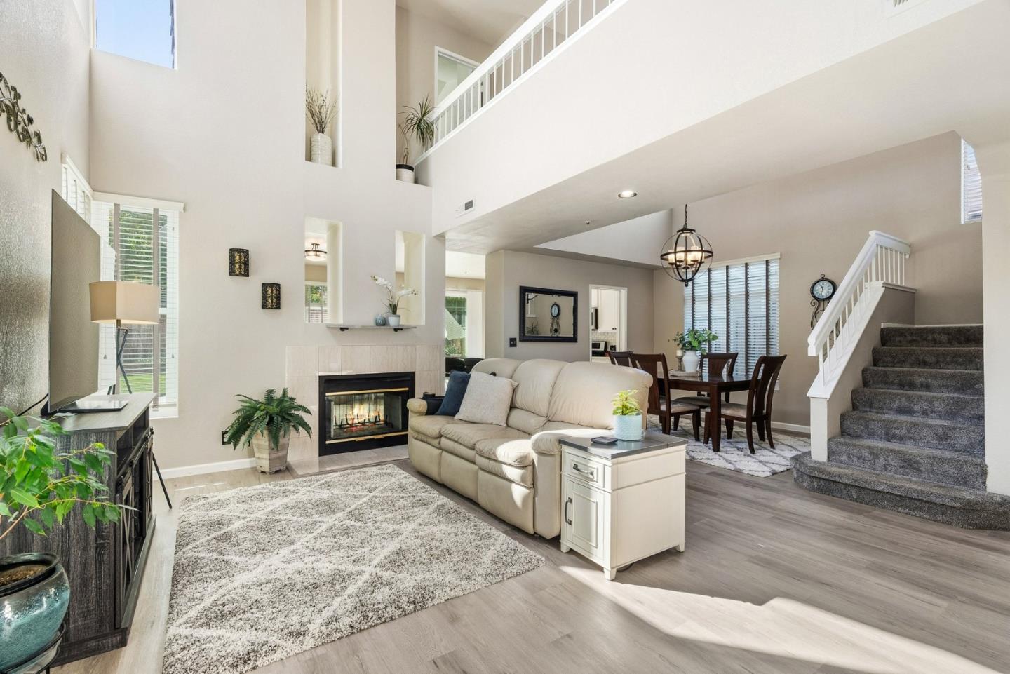 Two-story living room with a fireplace, neutral sofa, and carpeted staircase beside the dining area.