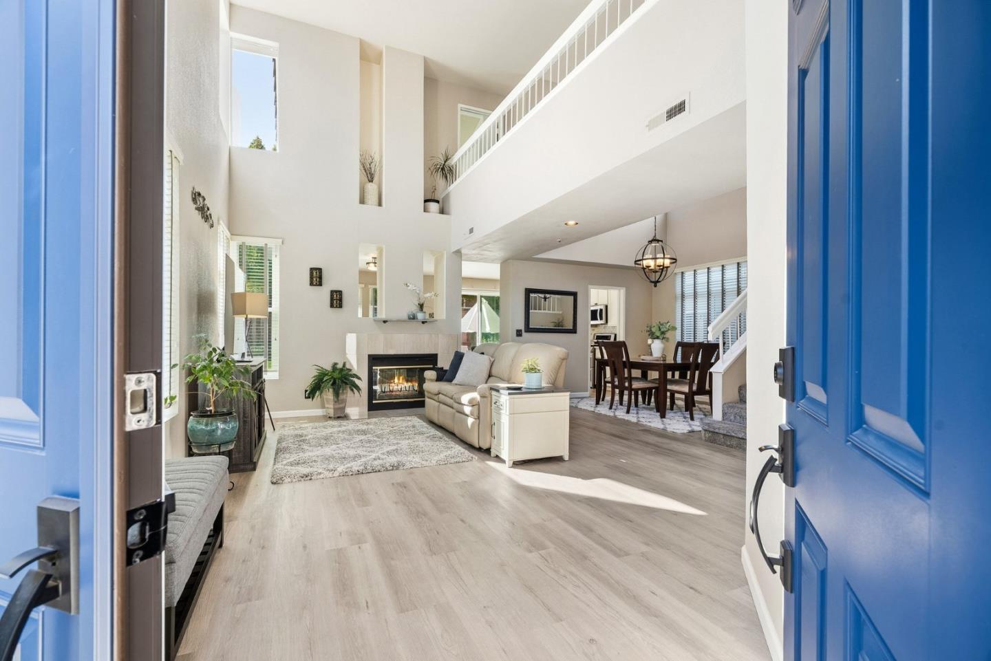 Two-story living room with a fireplace, vaulted ceiling, and dining area, viewed through a blue front door.