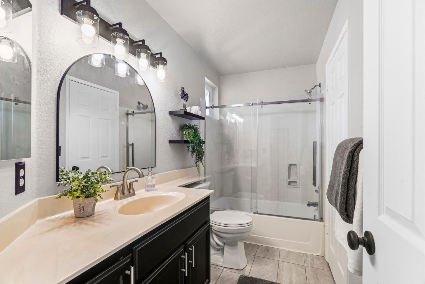 Bathroom with a dark vanity, arched mirror, and glass-enclosed tub-shower.
