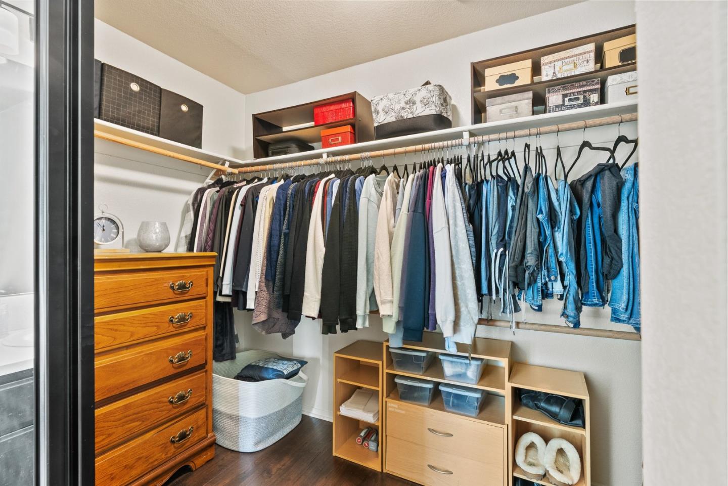 Walk-in closet with hanging clothes, wooden storage cubbies, and a chest of drawers.