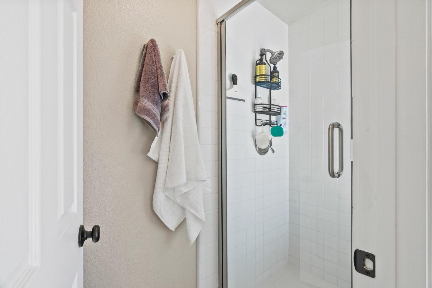 White tiled walk-in shower with a glass door and towels hanging beside it.