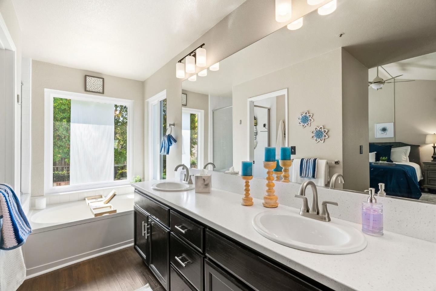 Bathroom with a dark double vanity, two sinks, and a soaking tub beneath a wide window.