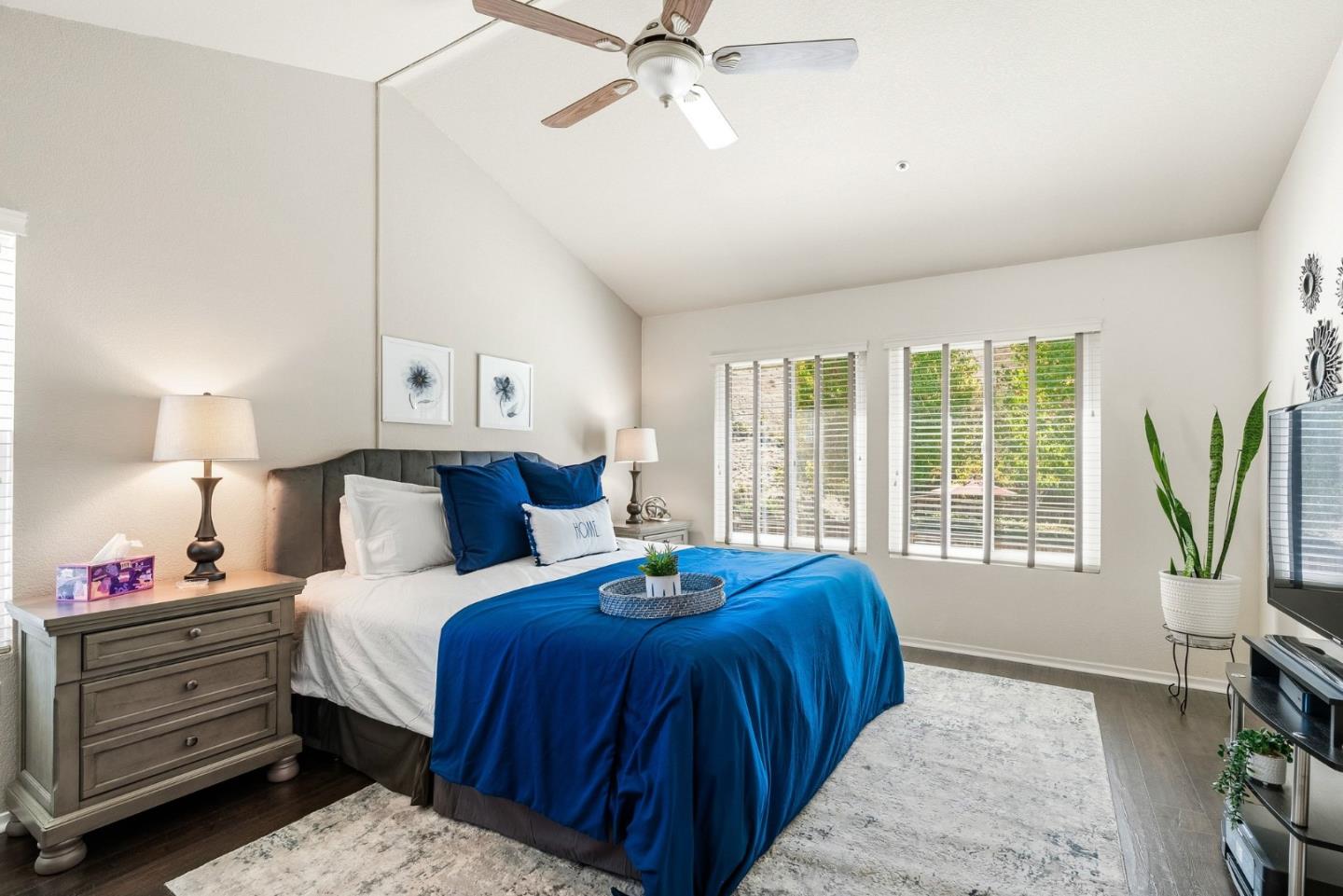 Furnished bedroom with vivid blue bedding, a gray headboard, wide windows, and a ceiling fan.