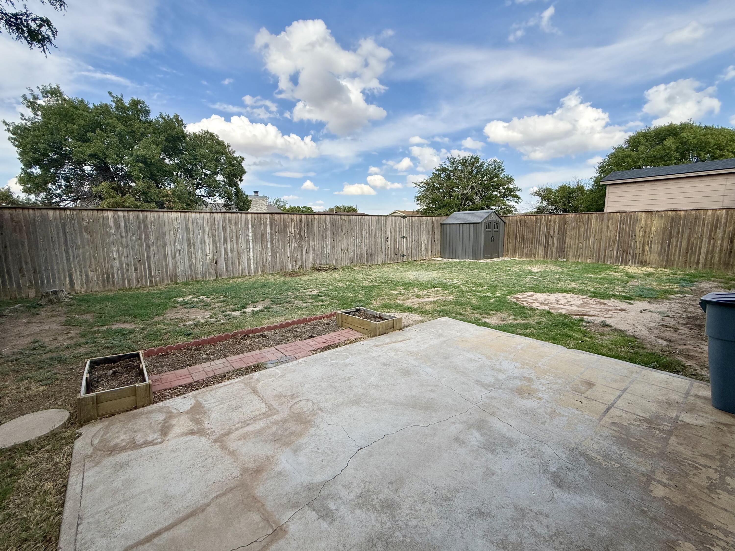 Fenced backyard with a concrete patio, raised garden beds, and a small storage shed.