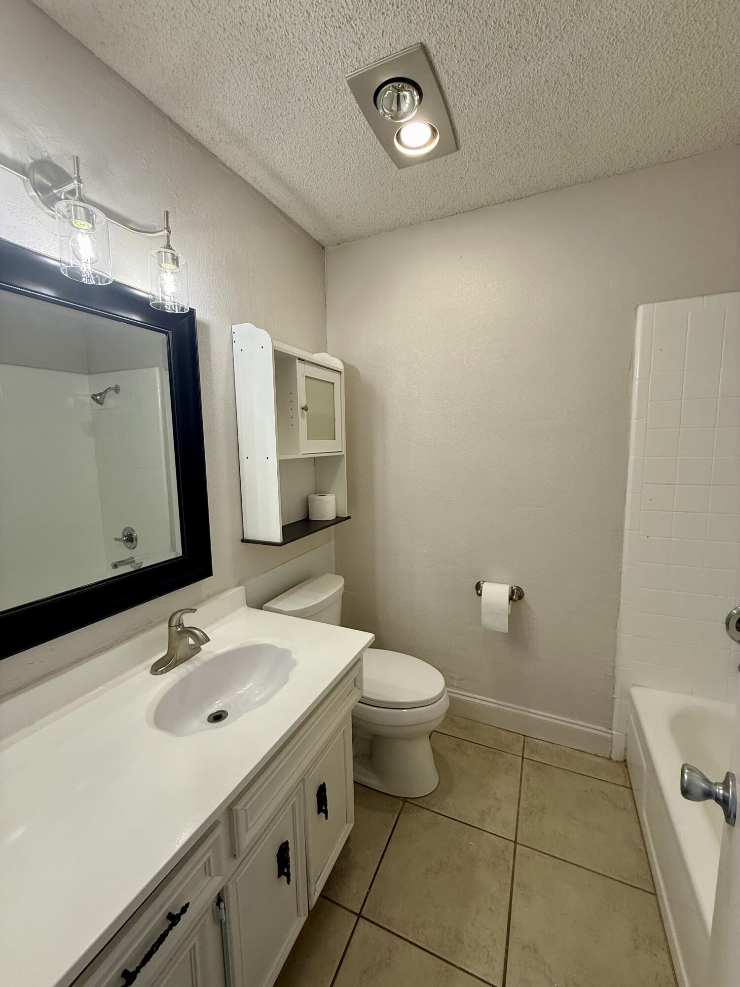 Bathroom with a white vanity, dark-framed mirror, toilet, and tiled bathtub surround.