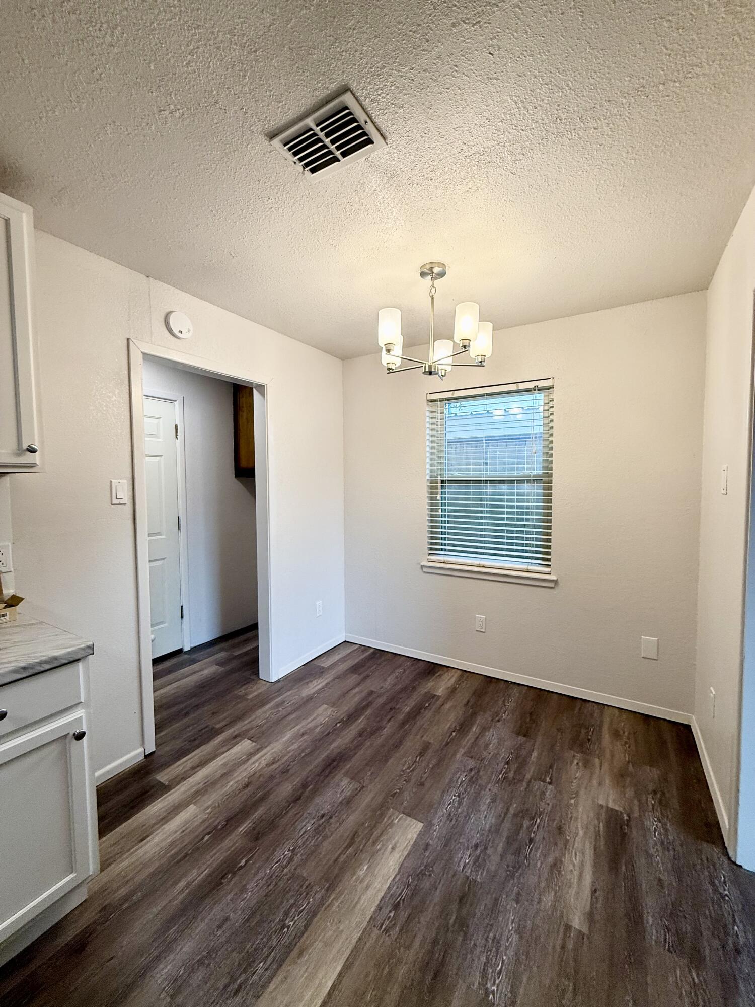 Empty dining area with dark wood-look flooring, window blinds, and a modern chandelier.