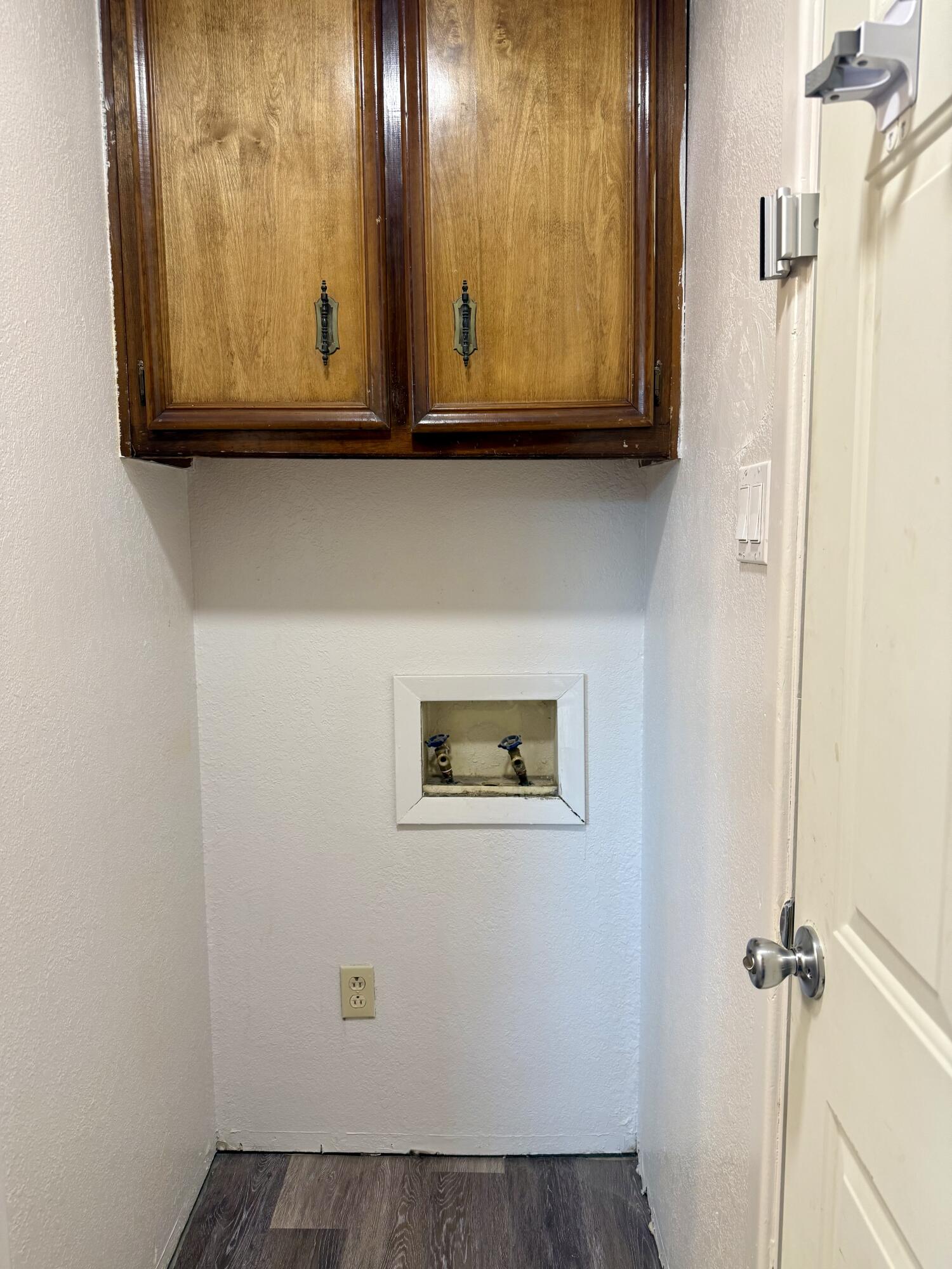 Laundry closet with washer and dryer hookups beneath overhead wooden cabinets.