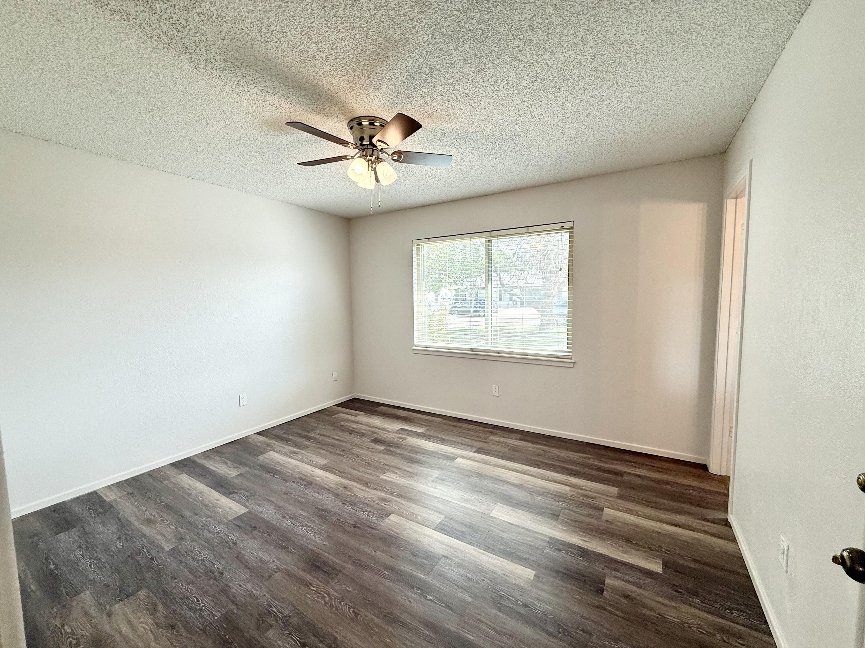 Empty bedroom with dark plank flooring, a ceiling fan, and a window with blinds.