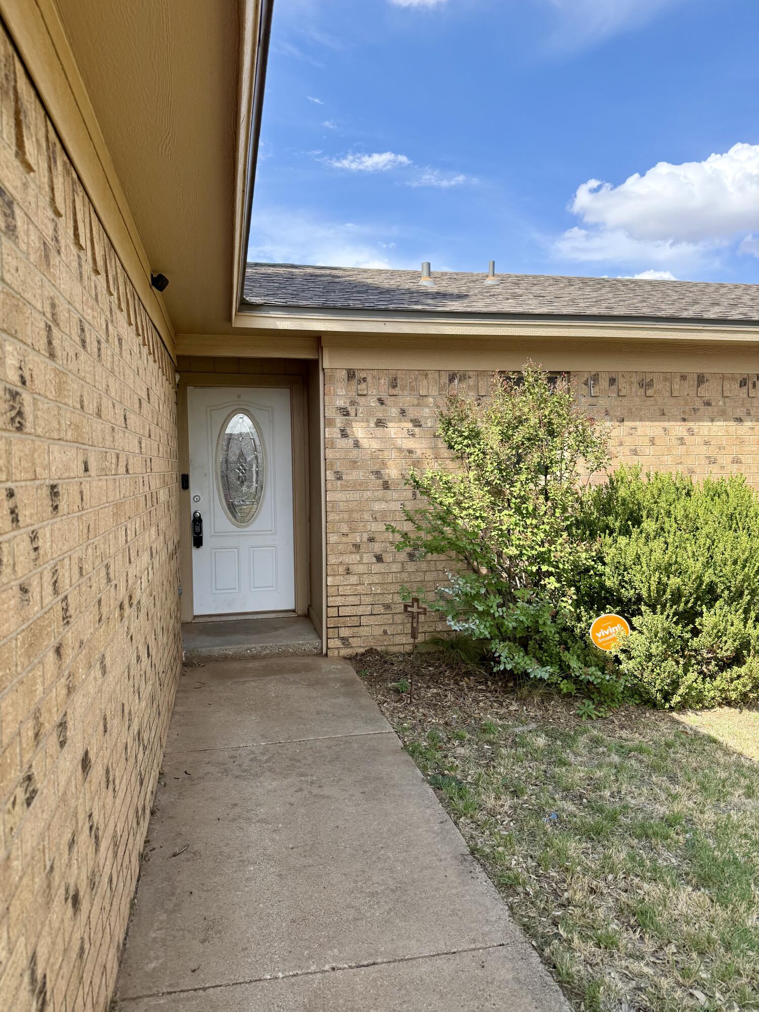 Recessed brick home entrance with a white oval-glass door, walkway, shrubs, and Vivint security sign.