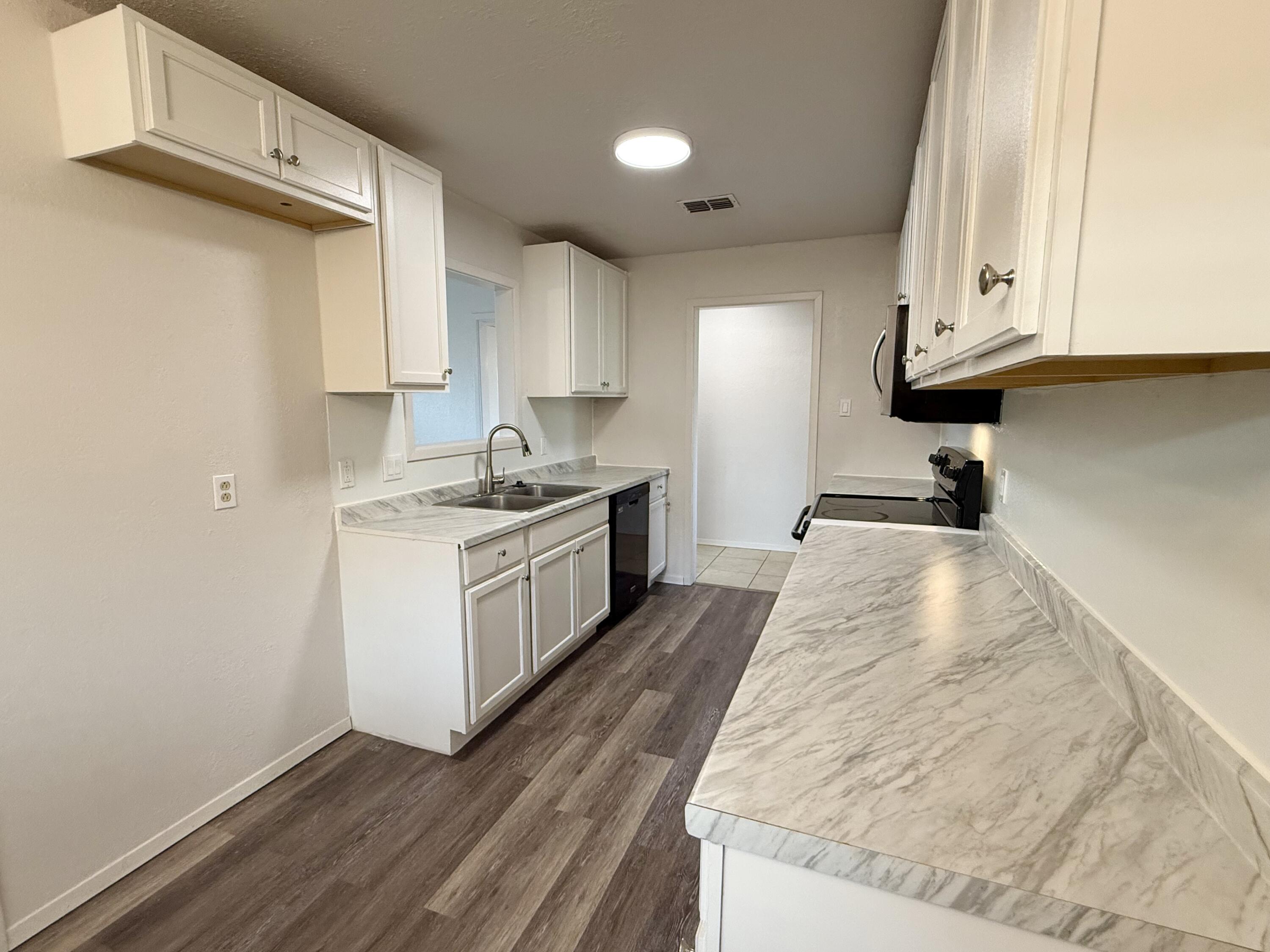 Galley kitchen with white cabinets, marble-look counters, and dark plank flooring.