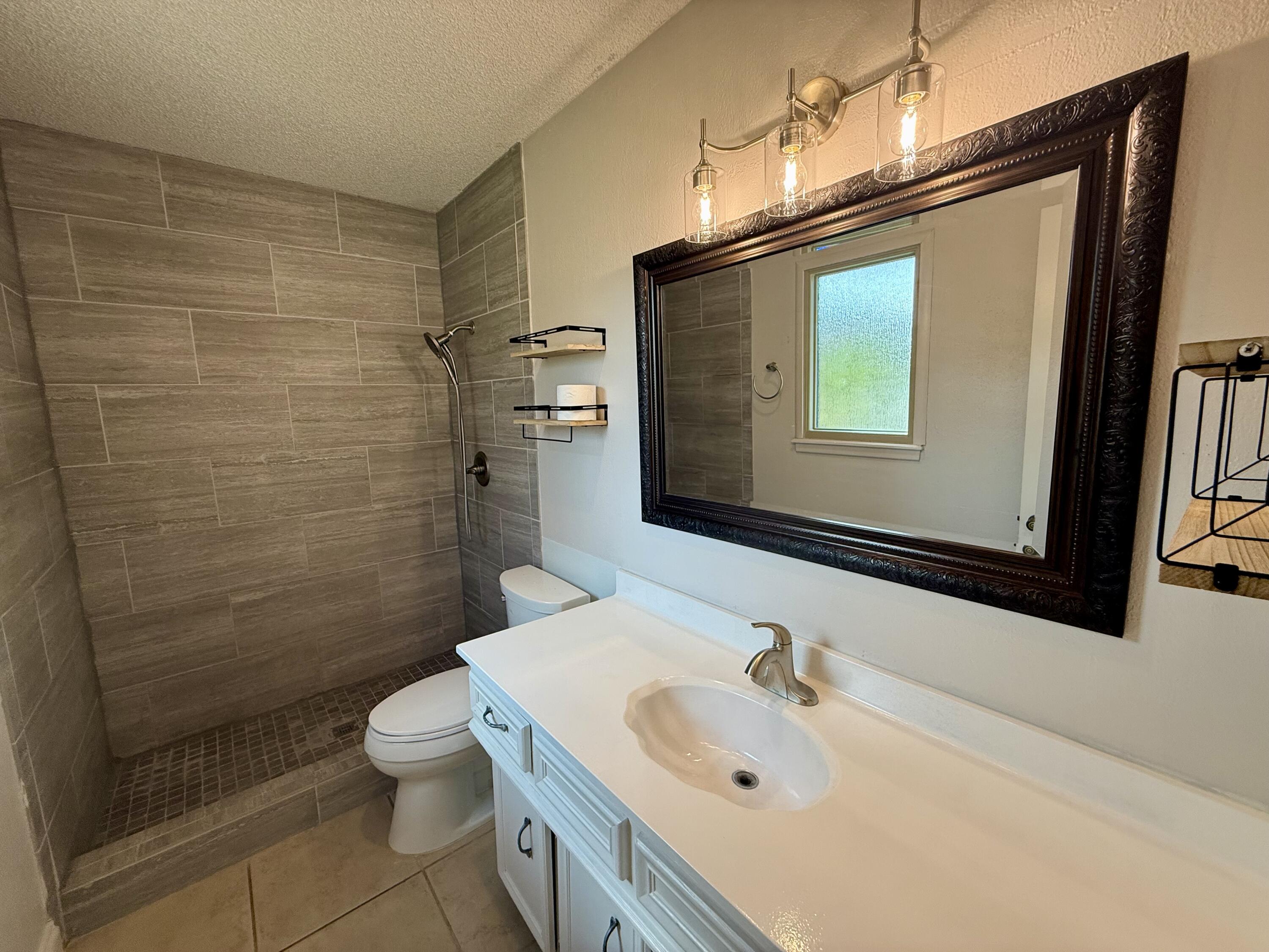Bathroom with a tiled walk-in shower, white vanity, and large ornate mirror.