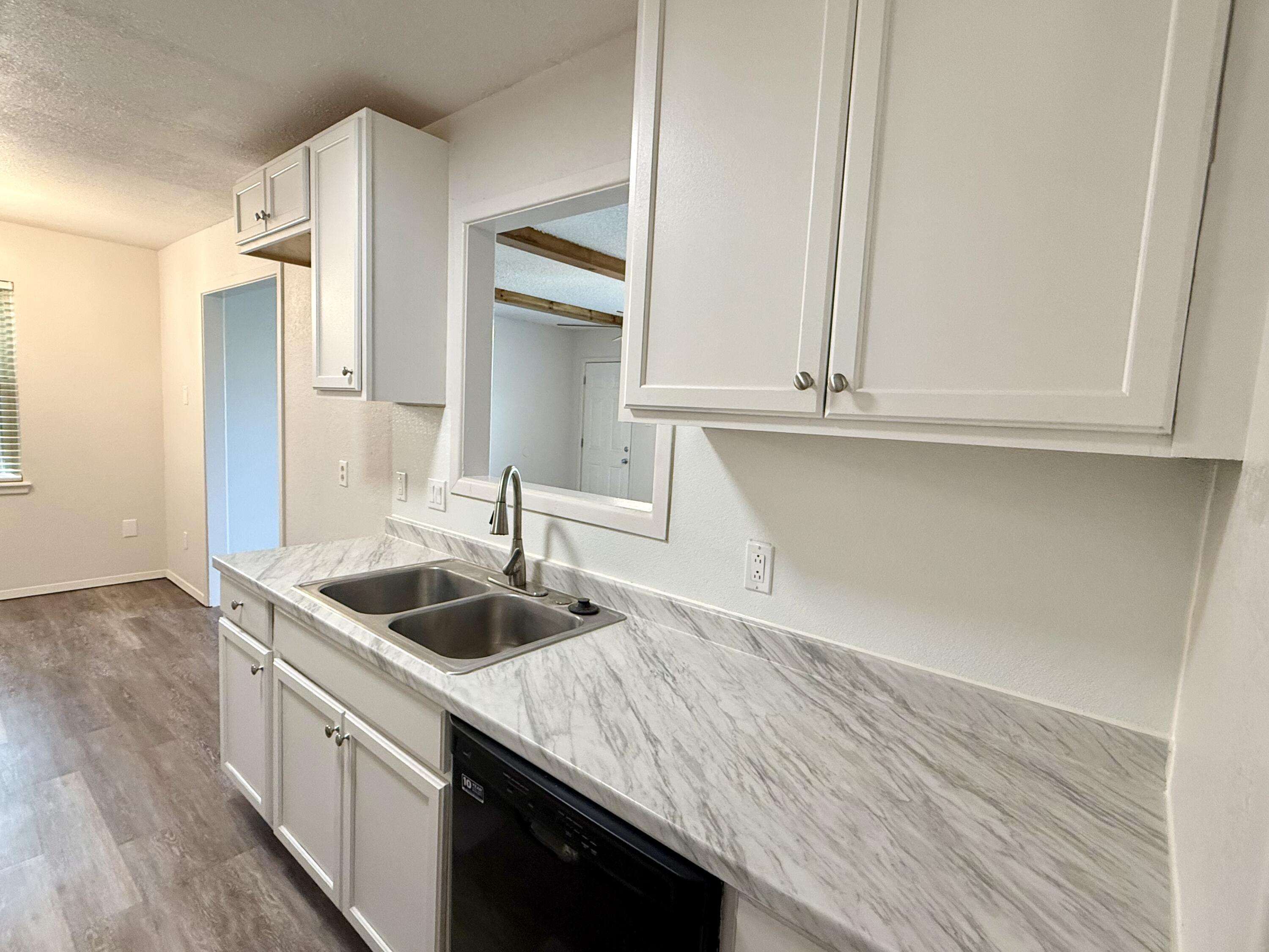 Kitchen with white cabinets, marble-look countertop, double sink, and black dishwasher.