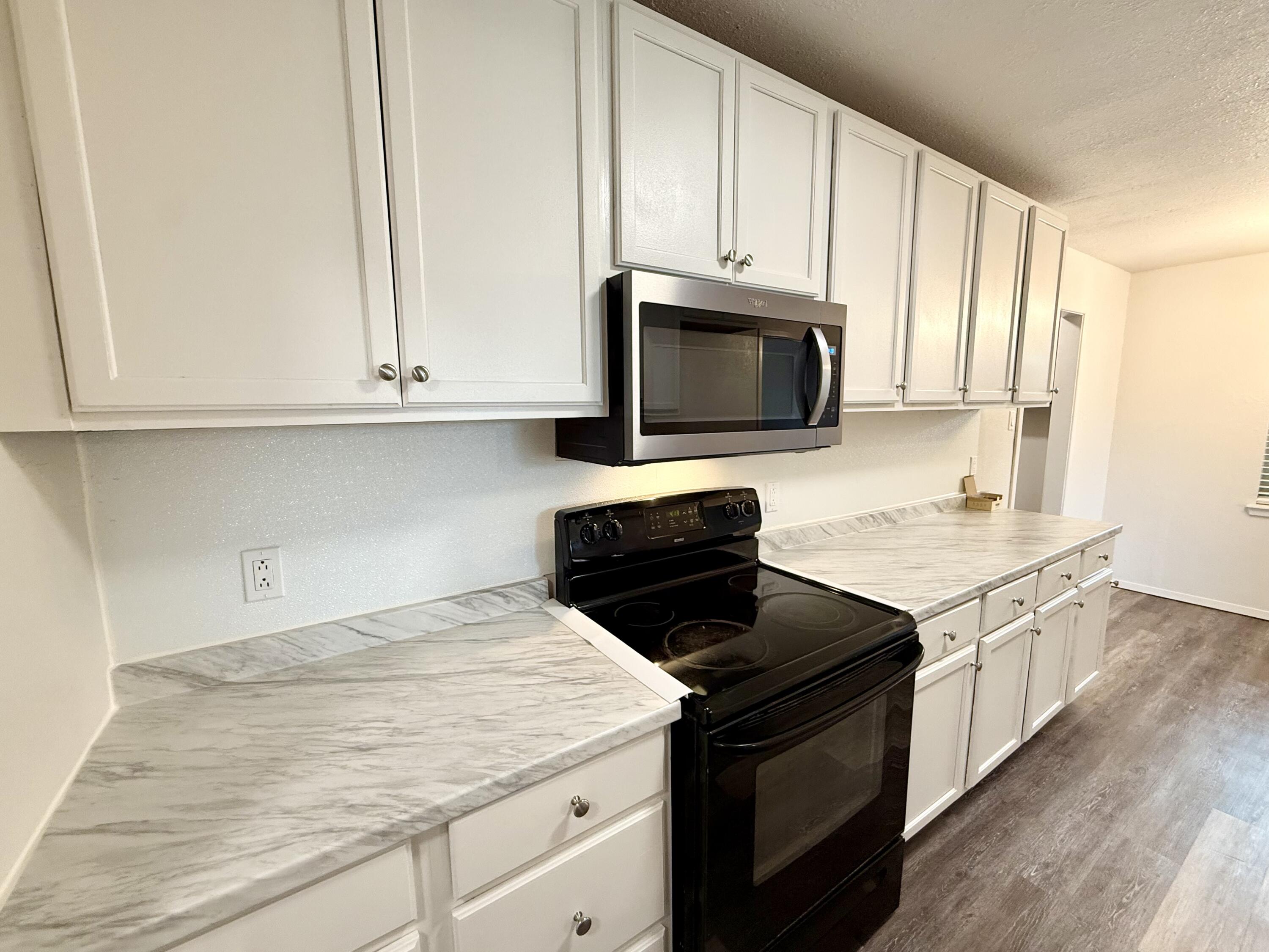 Kitchen with white cabinets, marble-look countertops, and black range beneath a stainless steel microwave.