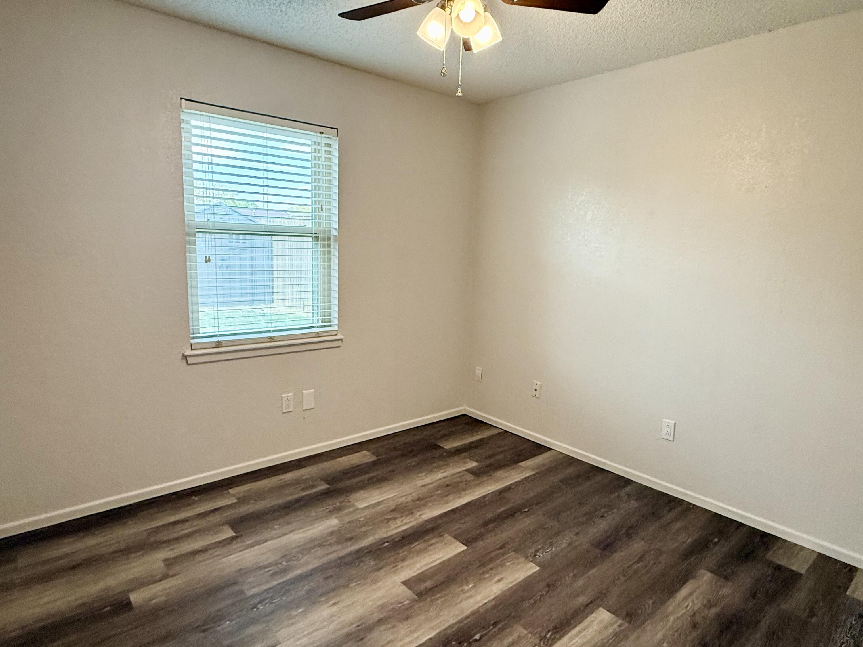 Empty room with dark plank flooring, a window with blinds, and a ceiling fan.