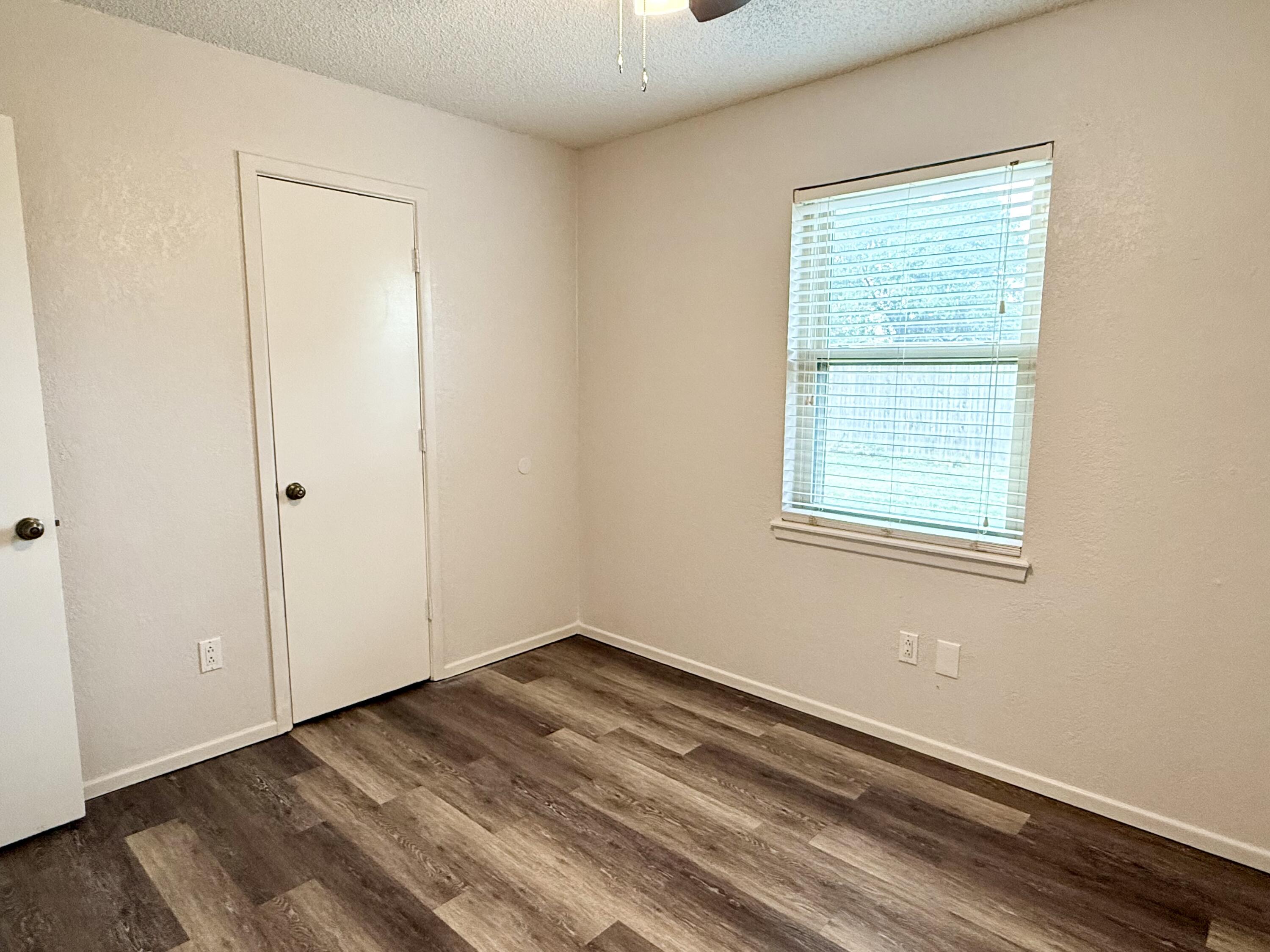Empty room with dark plank flooring and a window with white blinds.