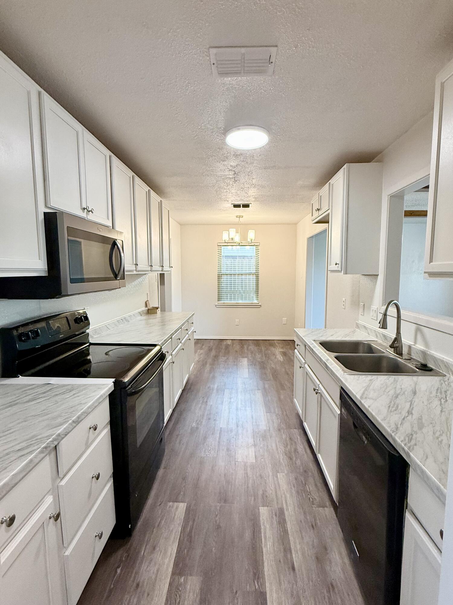 Galley kitchen with white cabinets, marble-look counters, a double sink, and dark appliances.