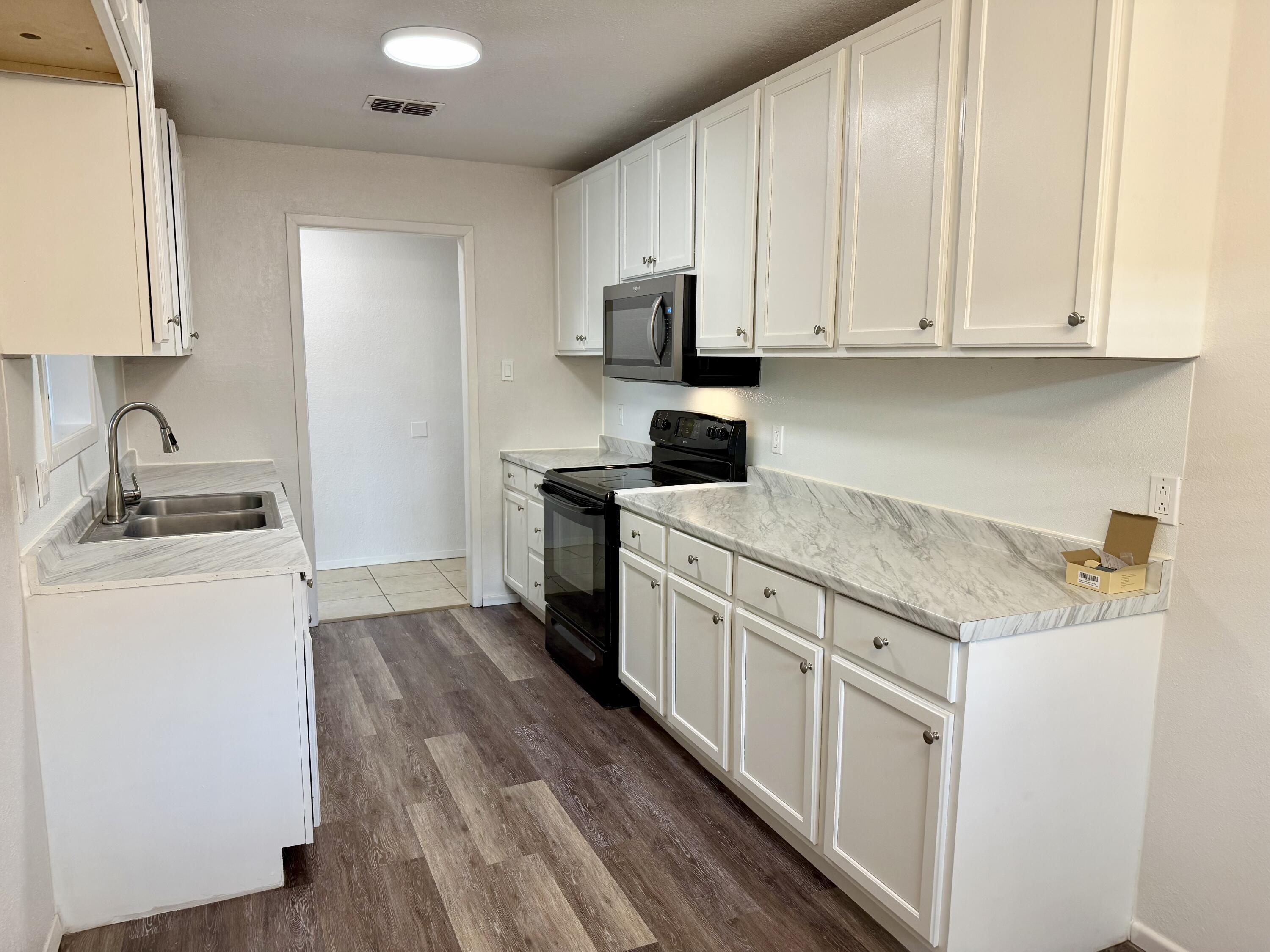 Kitchen with white cabinets, veined countertops, a double sink, and black appliances.