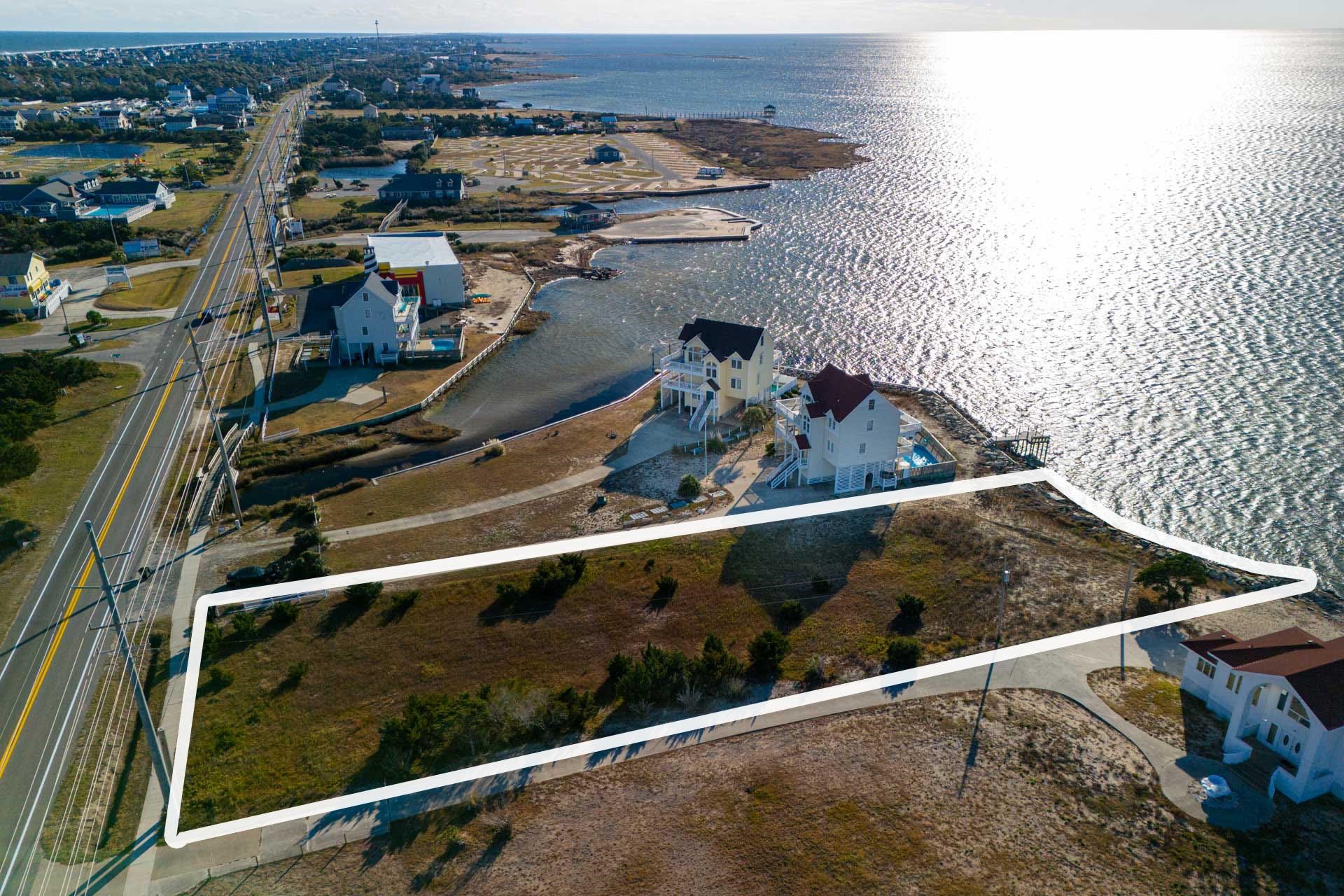 Outlined vacant waterfront parcel beside Highway 12, with coastal homes and water nearby.
