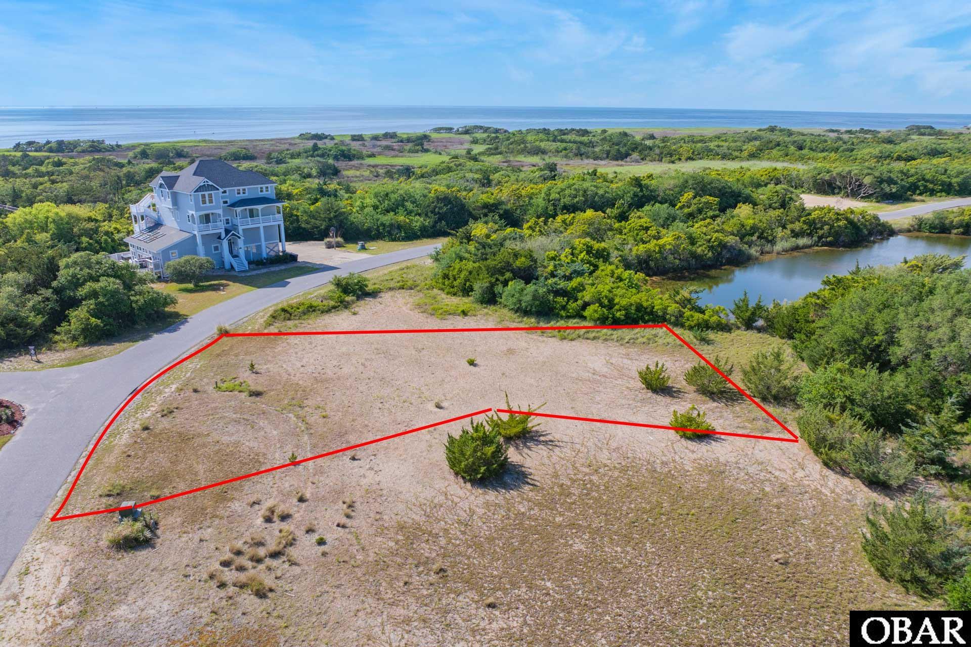 Vacant coastal lot outlined in red, with ocean views and a neighboring house nearby.