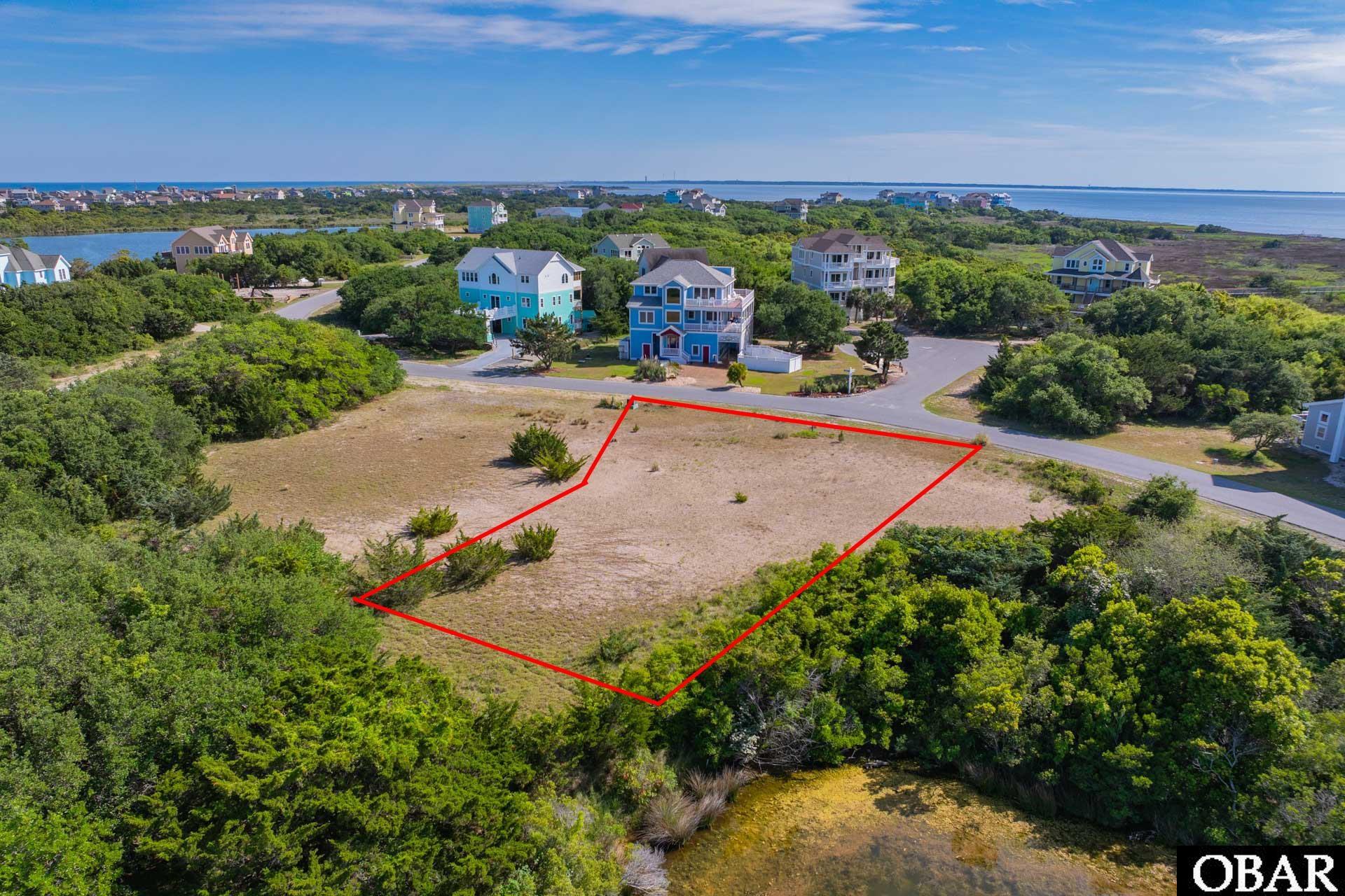 Aerial view of a vacant lot outlined in red, with coastal water and homes in the distance.