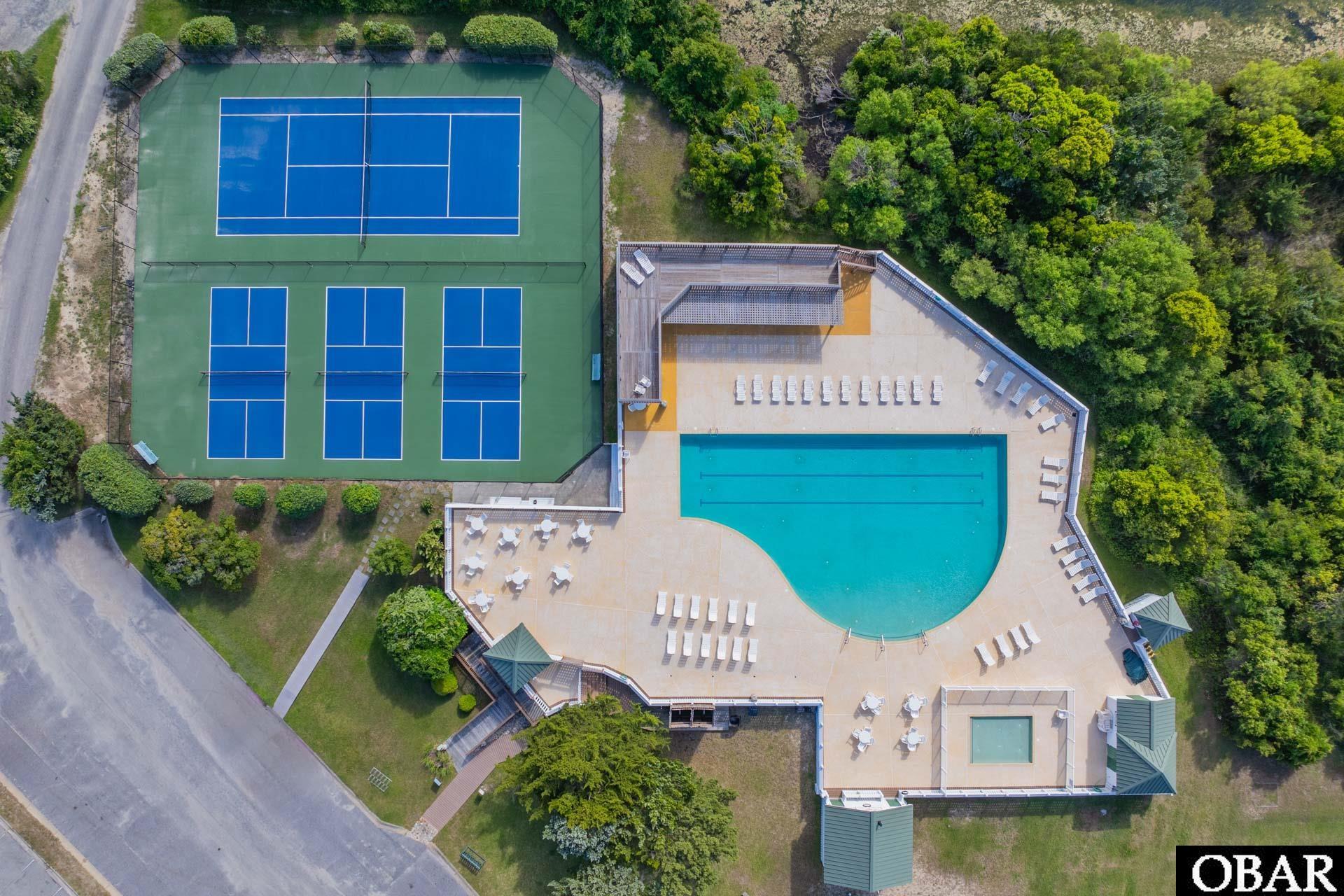 Aerial view of a community pool and tennis courts surrounded by trees.