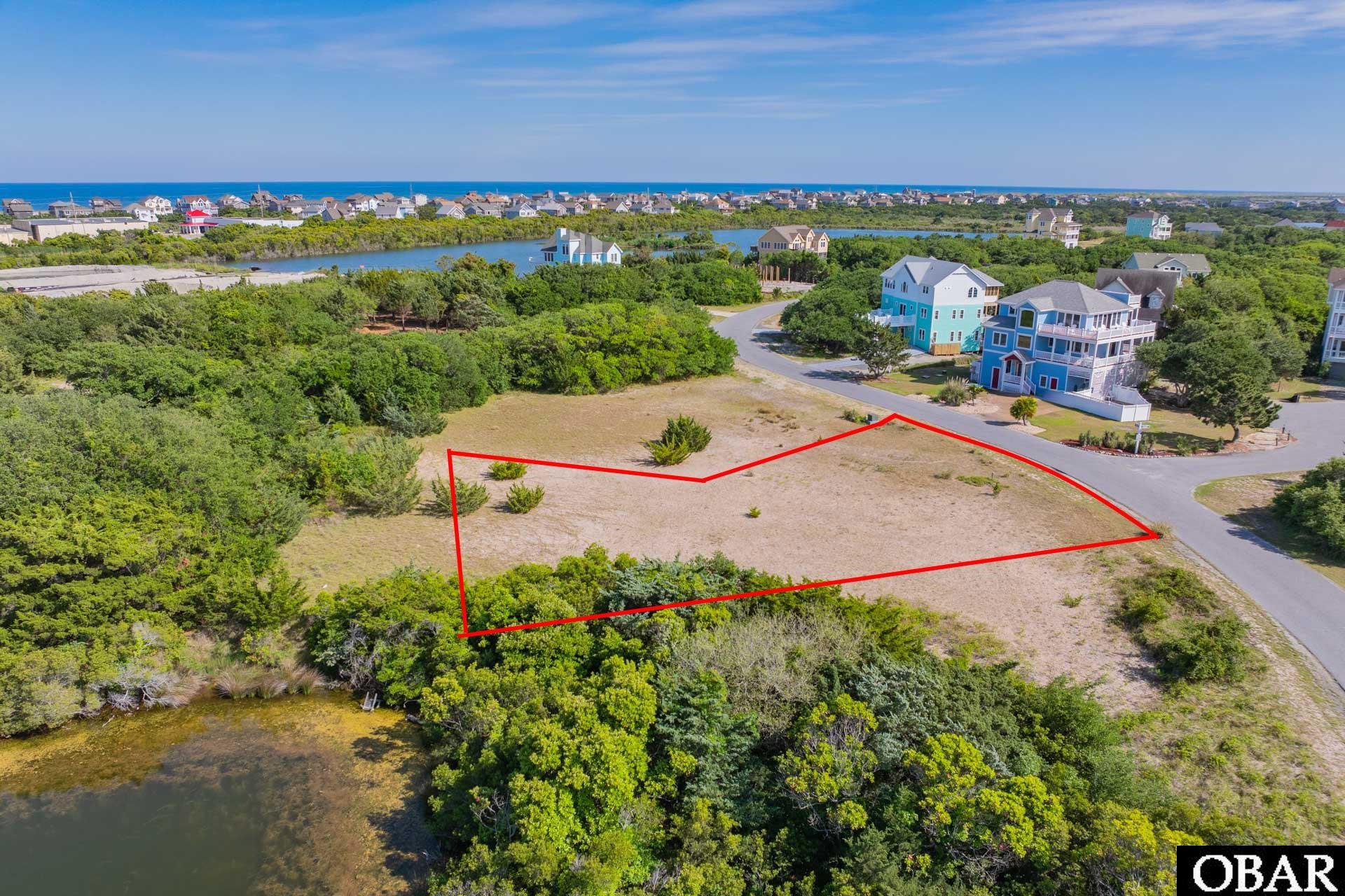 Vacant coastal lot outlined in red, with water and homes nearby.