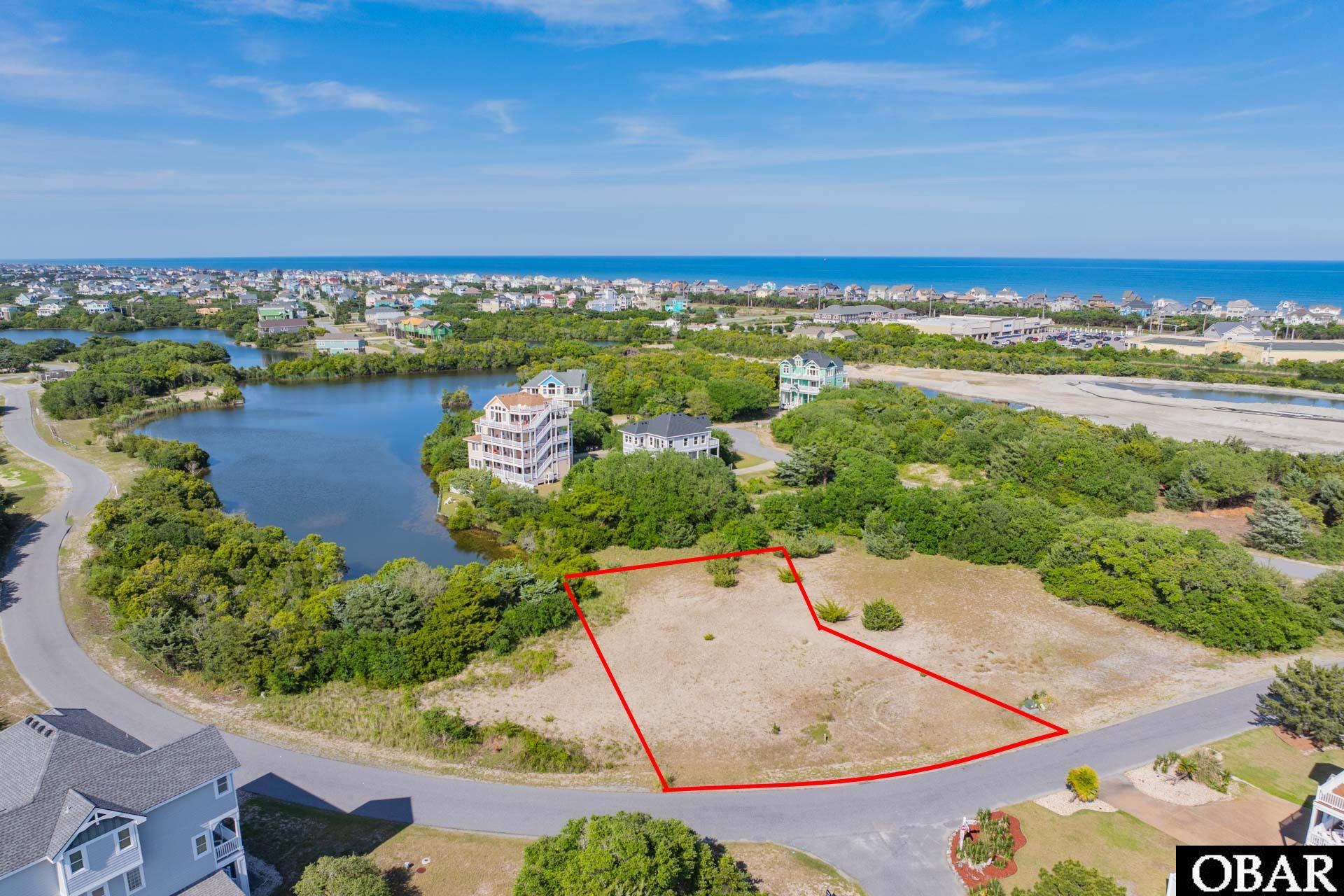 Vacant coastal lot outlined in red beside a pond, with homes and ocean in the distance.