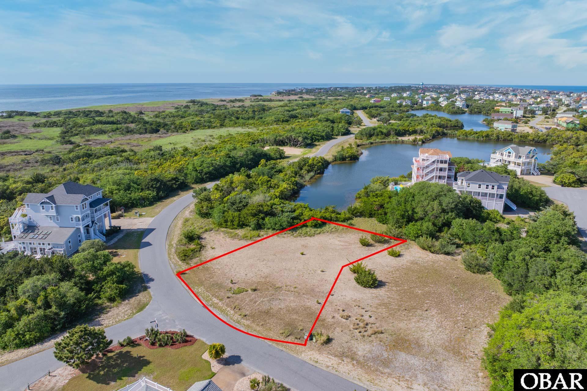 Vacant lot outlined in red beside a curving road, with ponds and the ocean in the distance.