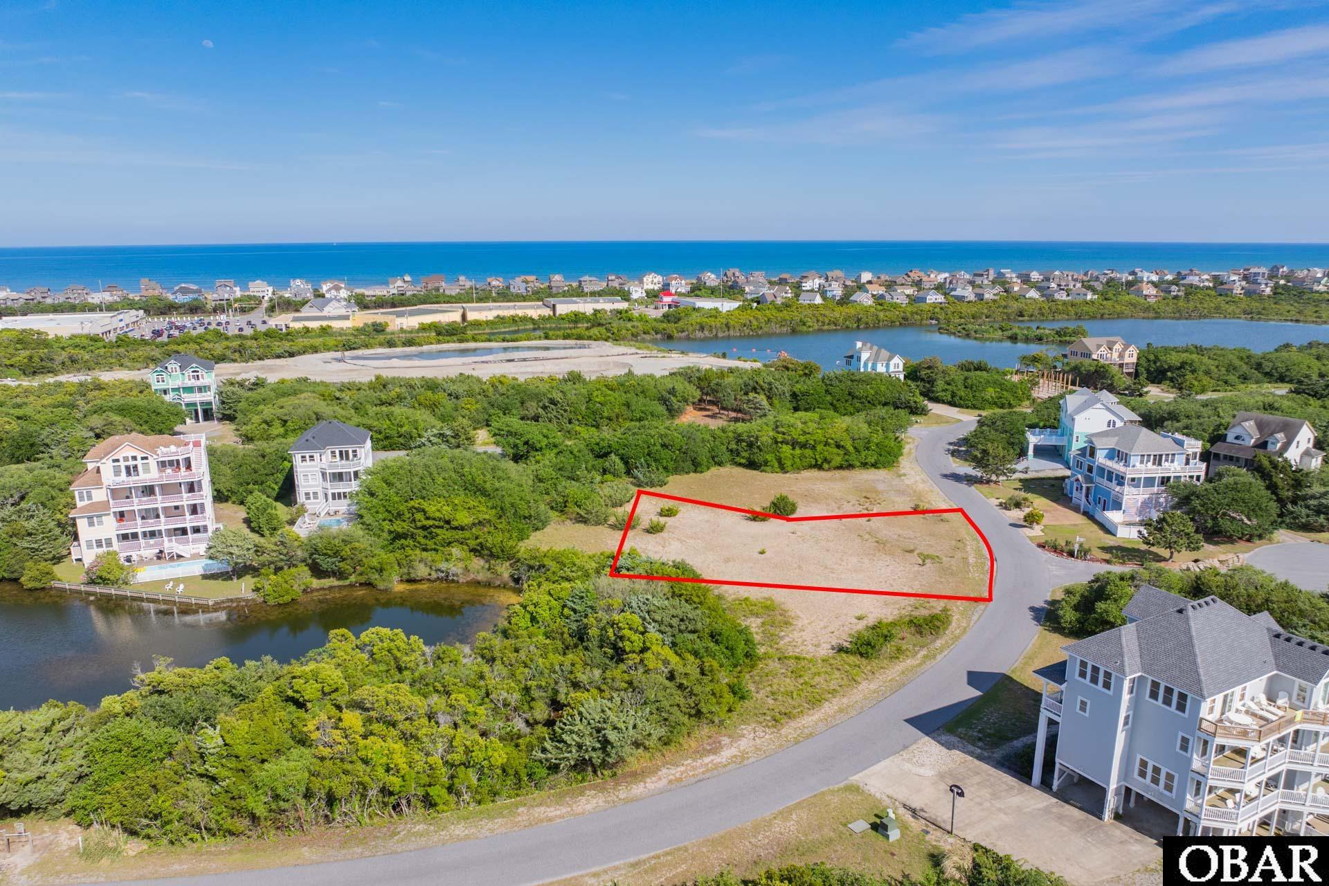 Vacant coastal lot outlined in red, with nearby homes, a pond, and ocean views.