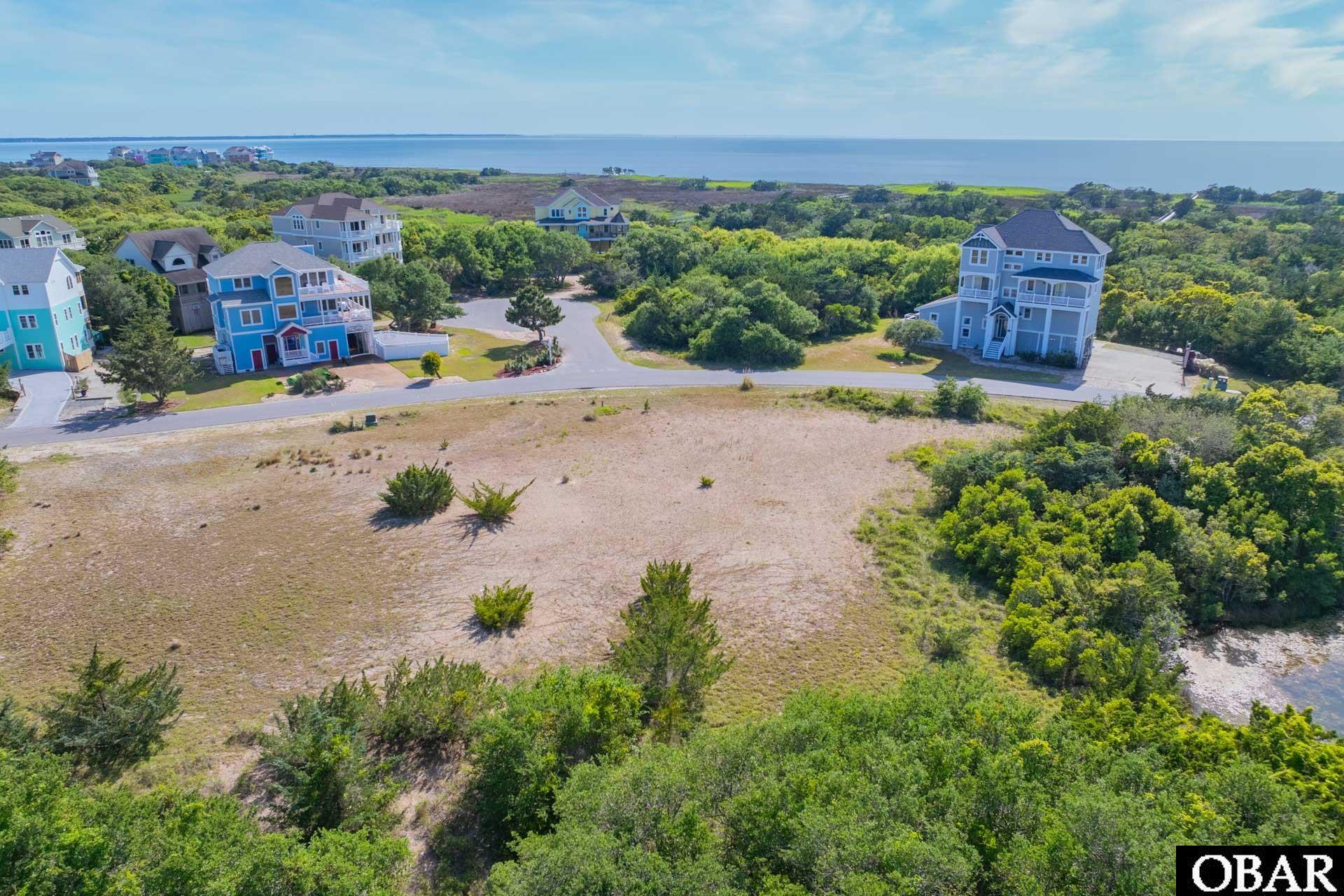 Aerial view of a vacant coastal lot near homes, with water visible beyond the neighborhood.