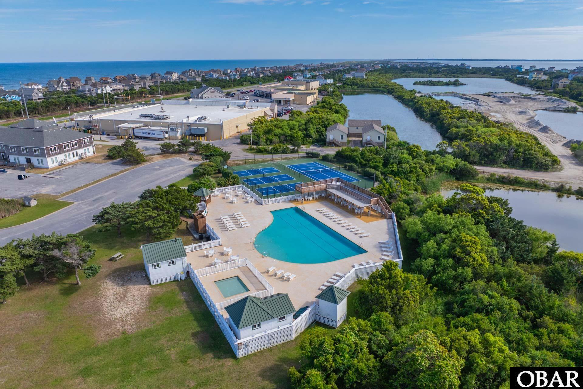 Aerial view of a coastal community pool and tennis courts, with the ocean and waterways beyond.