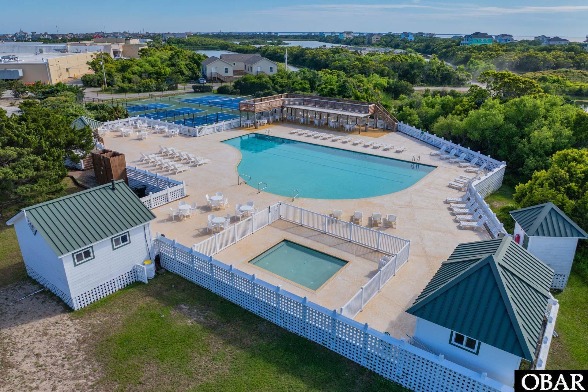 Community swimming pool and tennis courts with lounge chairs and shaded decks, viewed from above.