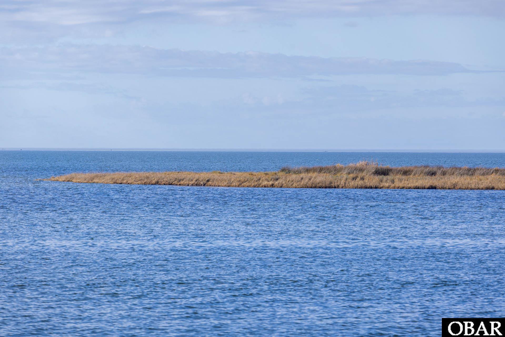 Grassy island lot edged by blue water beneath a cloudy sky.