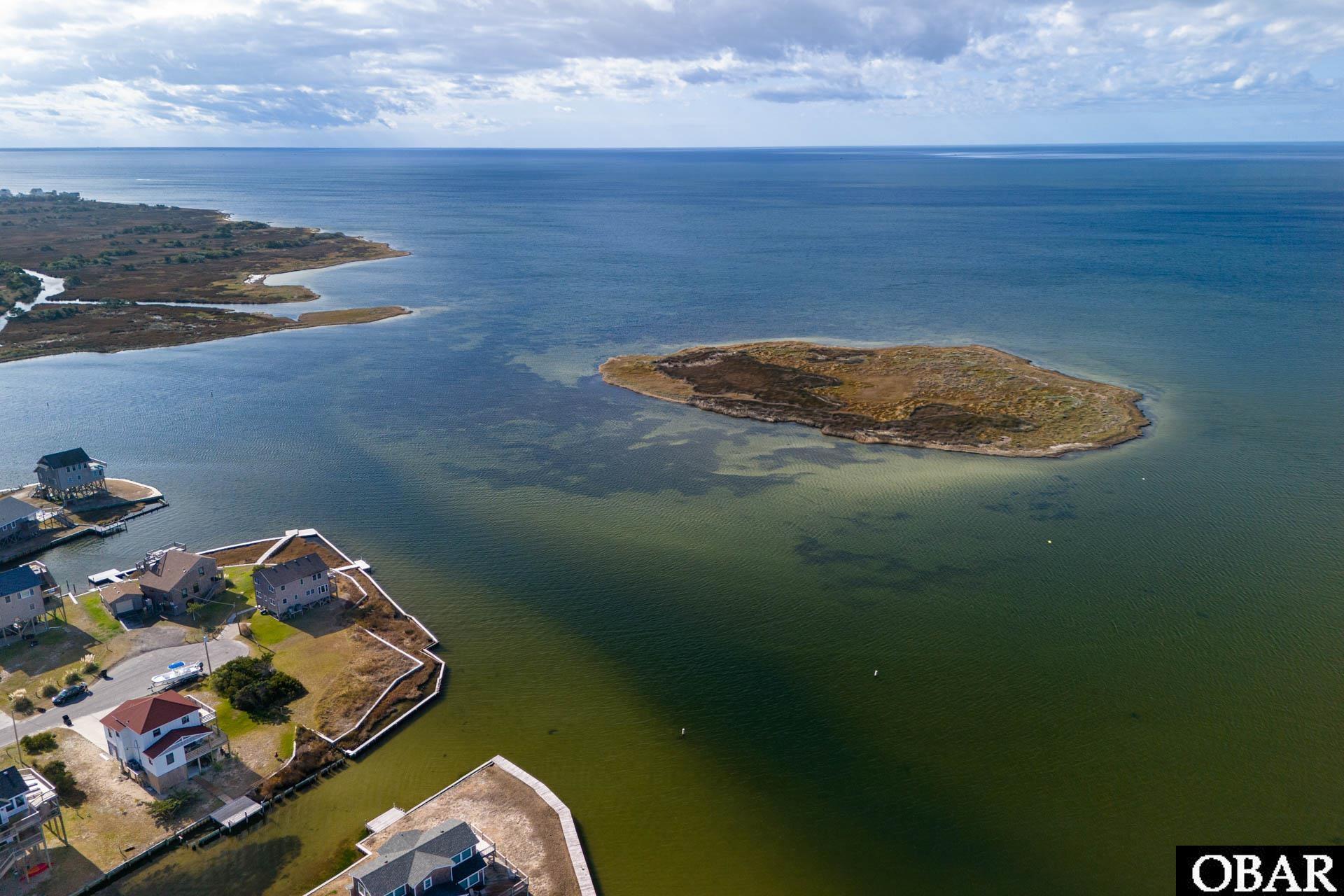 Aerial view of a marshy island lot surrounded by water, with homes along the nearby shoreline.