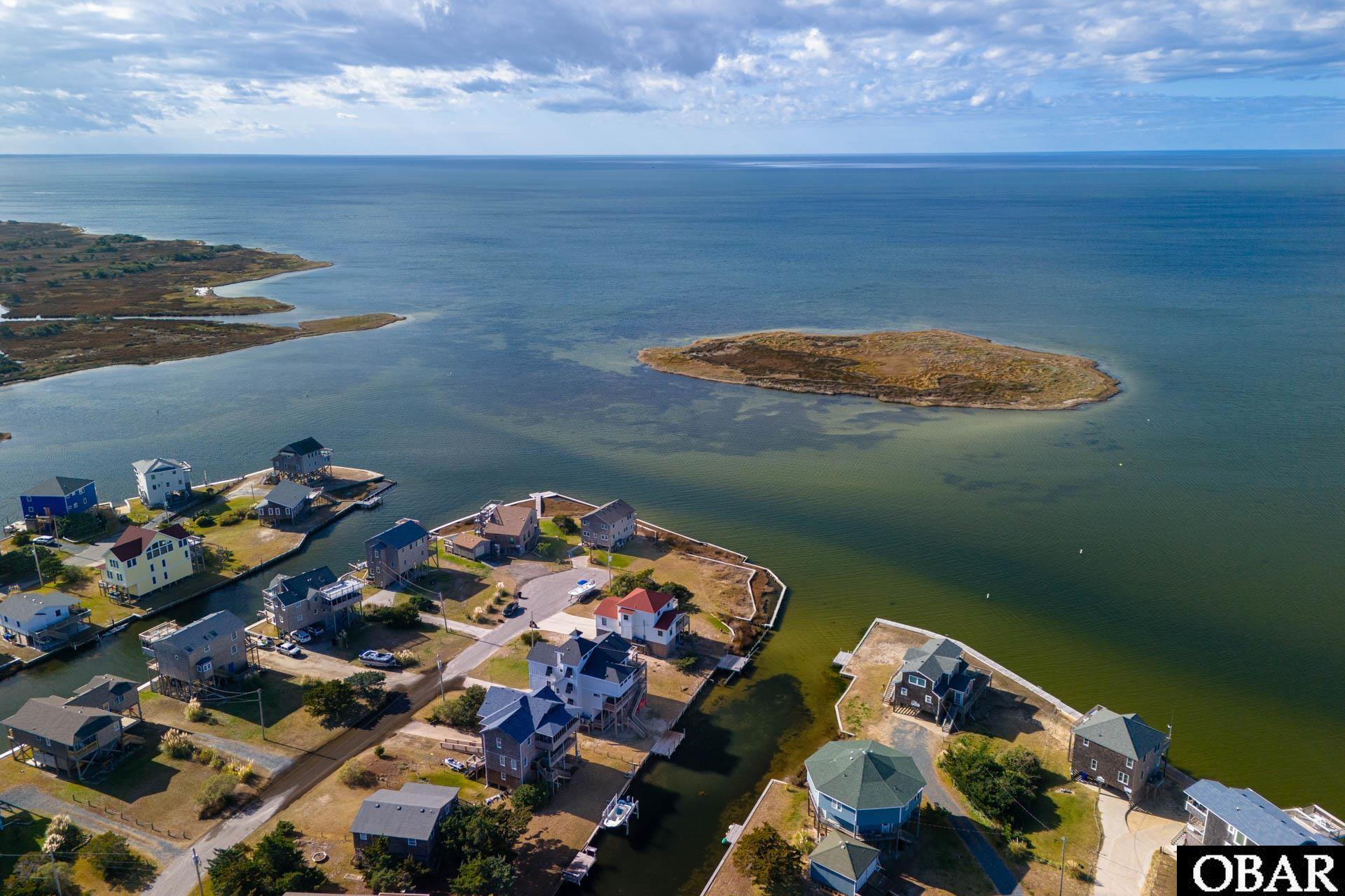 Aerial view of an undeveloped island in coastal water, with shoreline homes in the foreground.