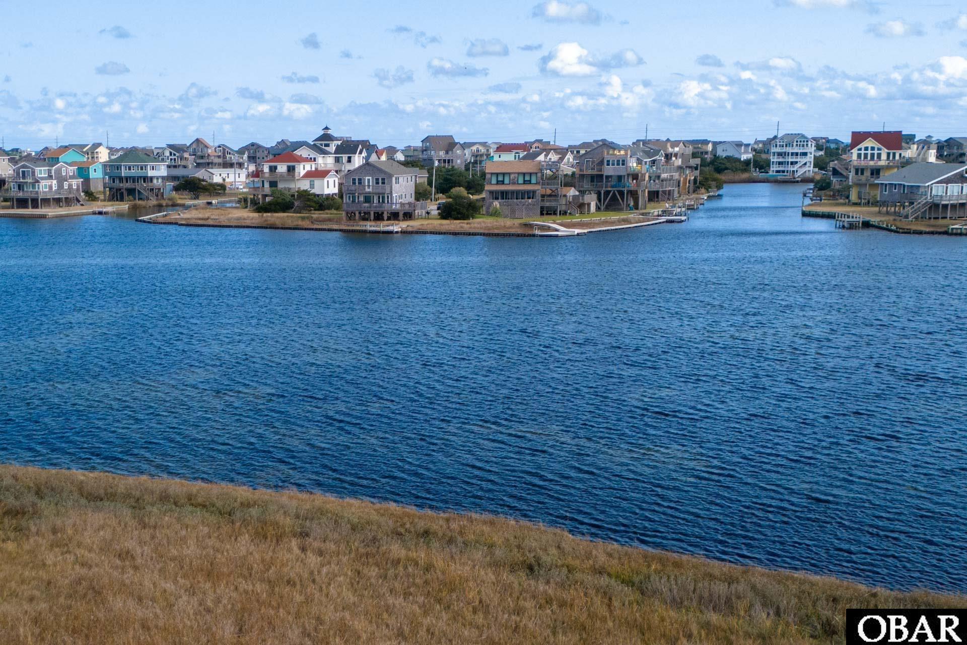 Grassy waterfront lot overlooking a broad waterway and a neighborhood of homes.