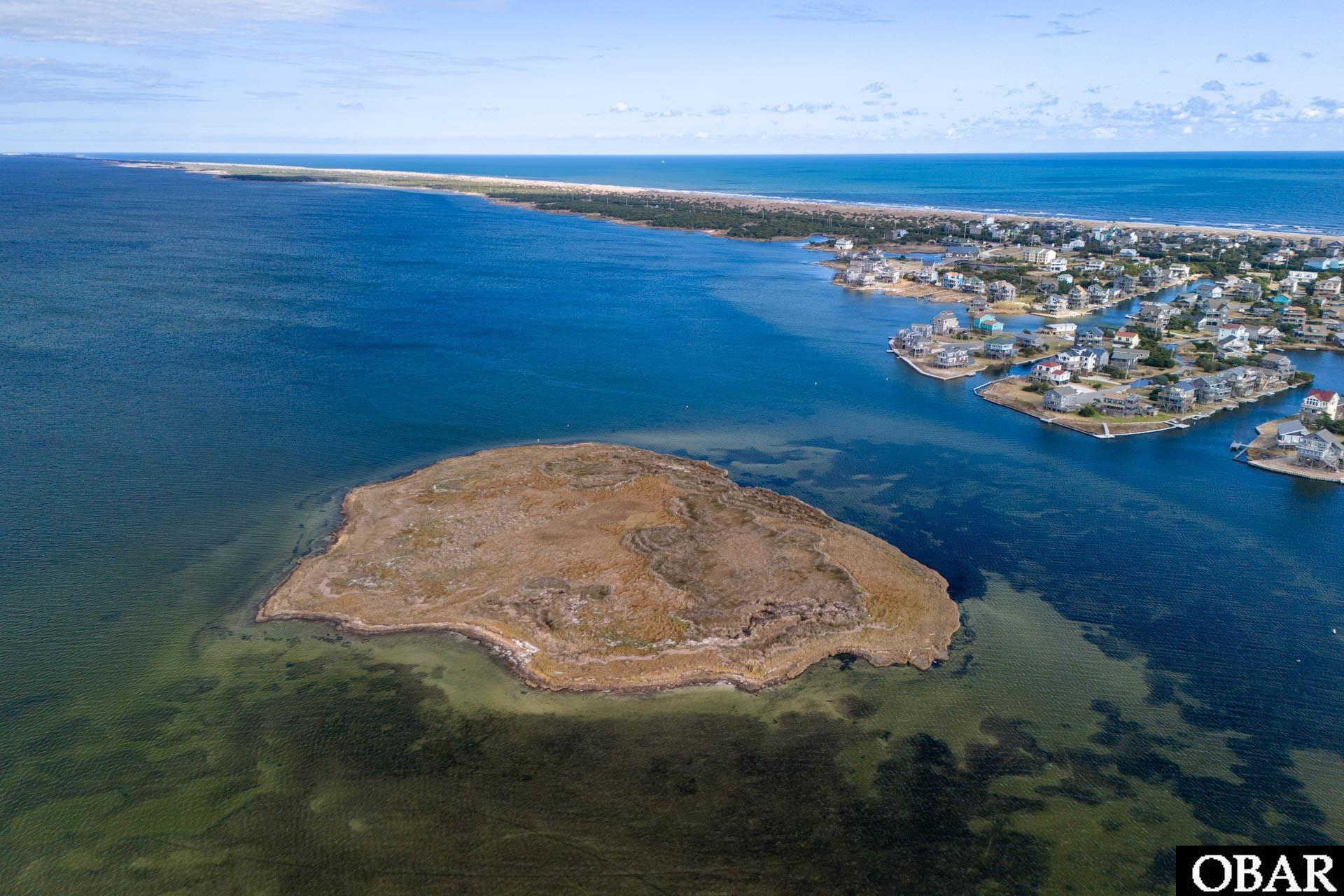 Aerial view of a marshy island lot surrounded by water, with Avon homes and the ocean beyond.