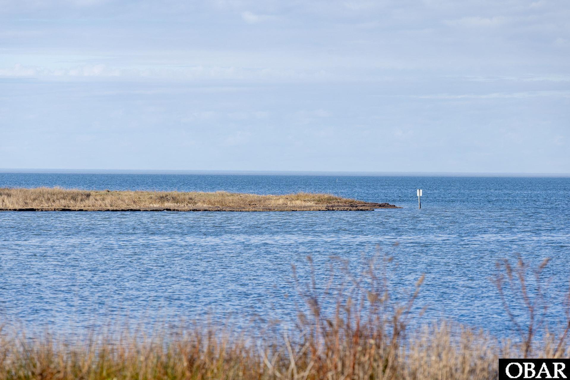 Grassy island lot extending into blue water beside a navigation marker.